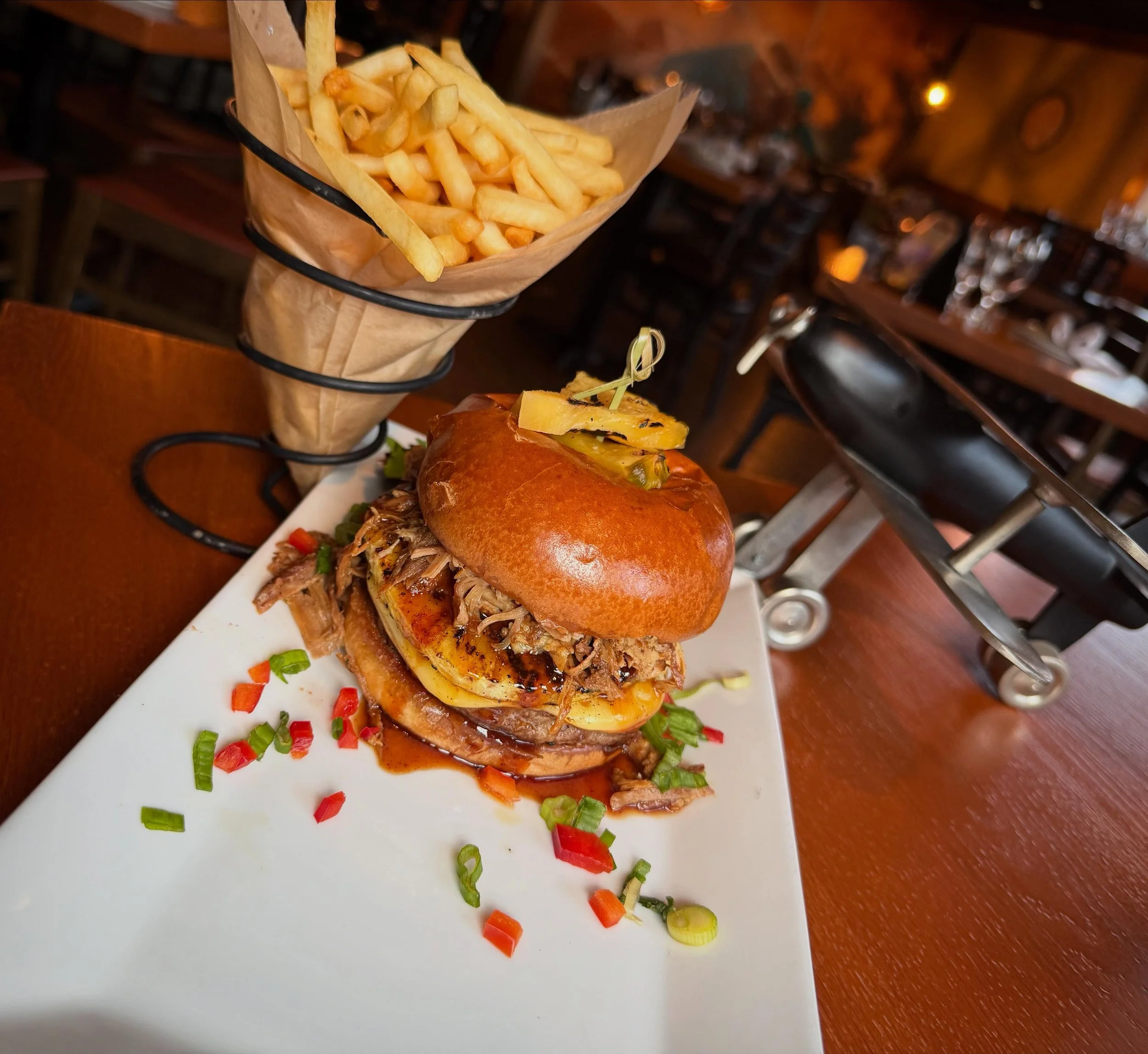 Pilots Maui Burger- Hand pressed angus beef on a toasted brioche bun, topped with grilled pineapple, kalua pulled pork, cajun mayo and crispy onion straws. Served with French cut fries