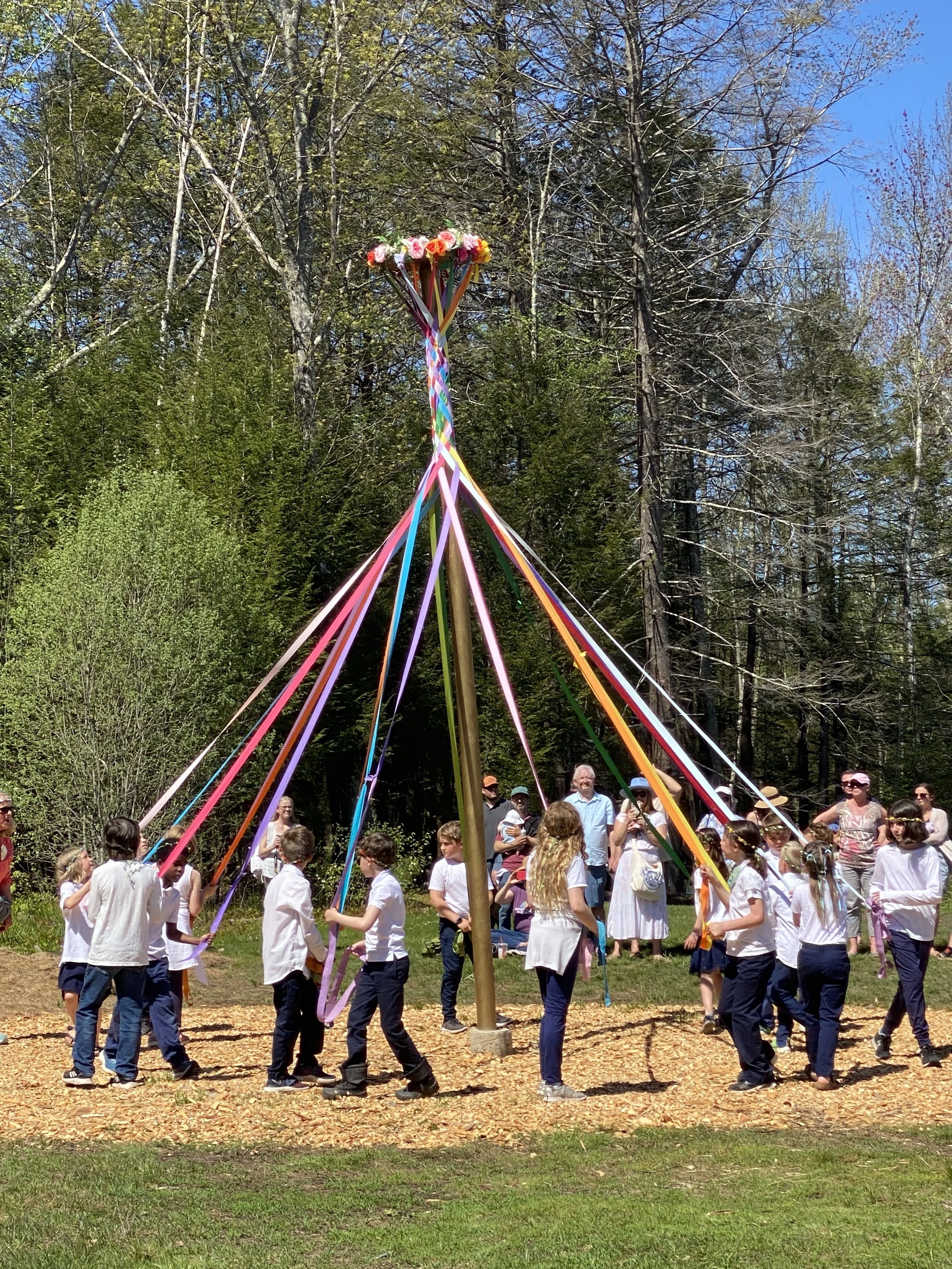 Children and adults participating in a maypole dance at Seacoast Waldorf School