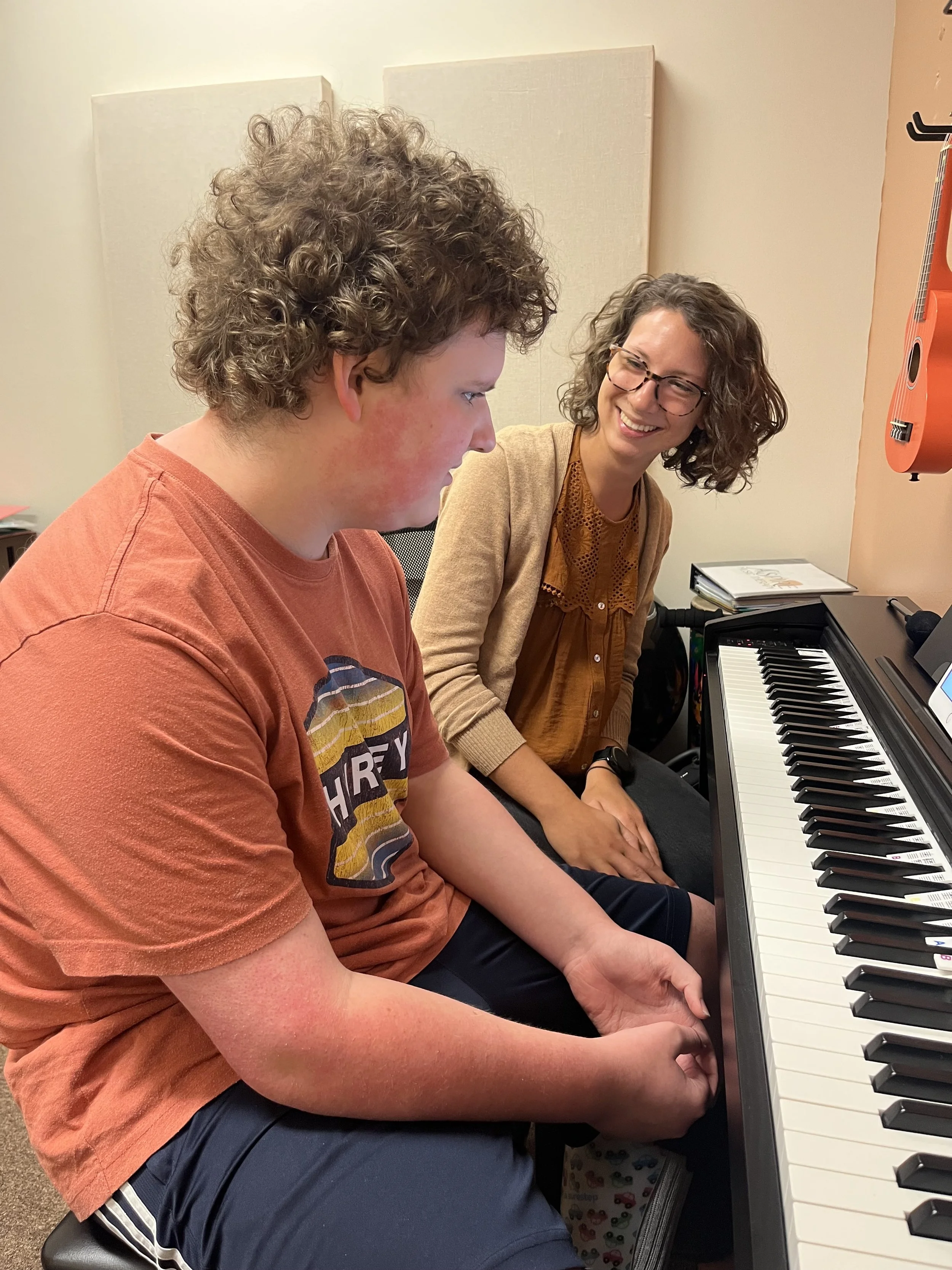 Teen with autism looking at piano during music therapy session with music therapy intern smiling at him