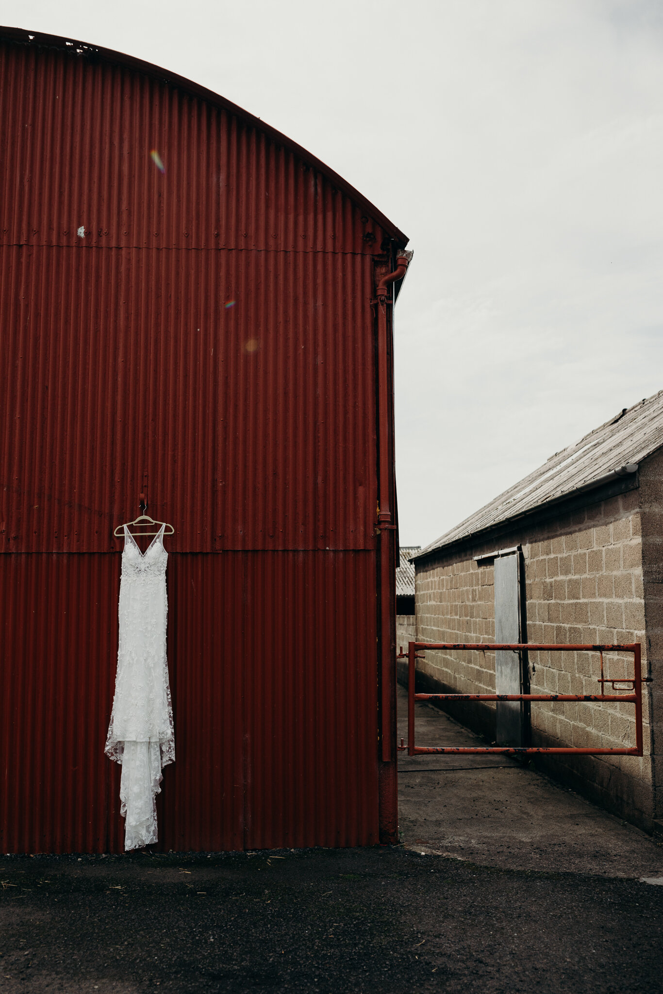 wedding photographer ayrshire photographs wedding dress hanging on the outside of red barn at dalduff farm wedding venue scotland