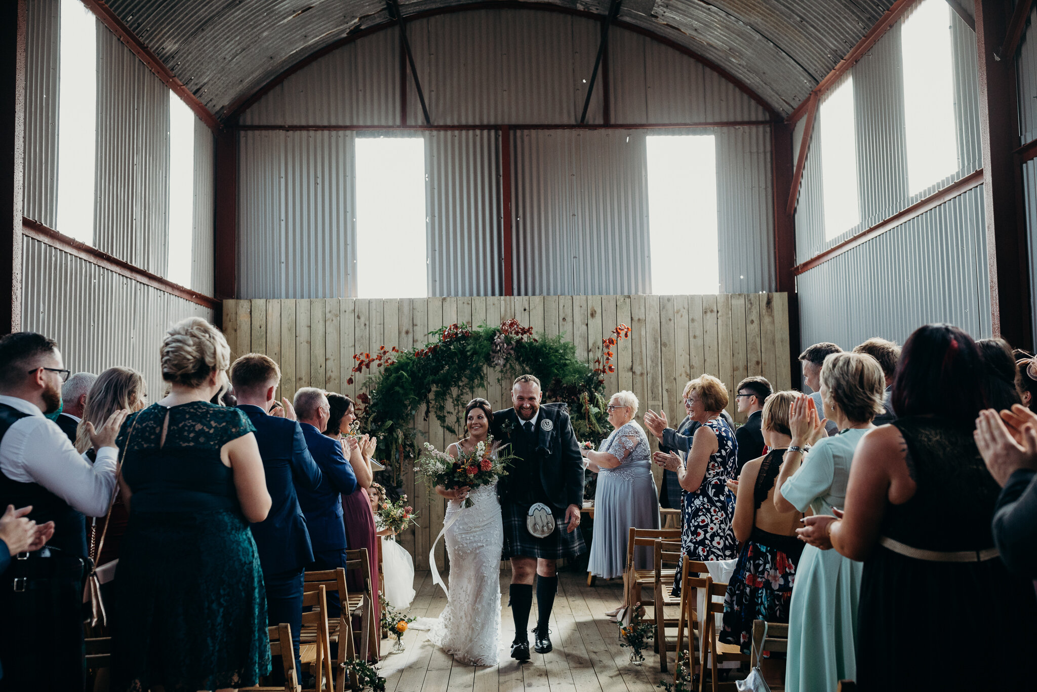 bride and groom walking down the aisle smiling at guests in barn outdoors at dalduff farm wedding photographed by wedding photographer ayrshire scotland