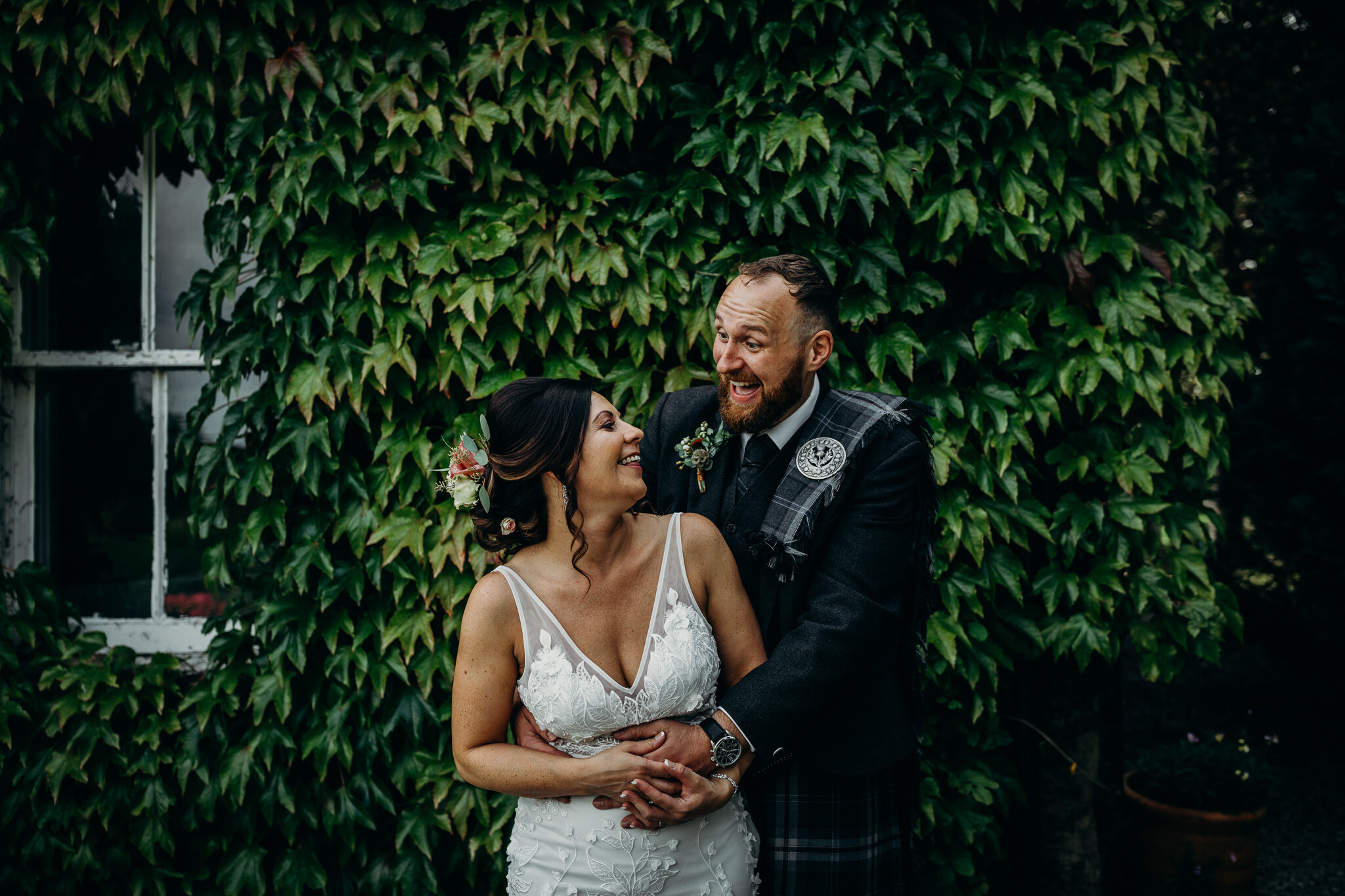 bride and groom hugging and smiling in front of wall covered in ivy outdoors at dalduff farm photographed by wedding photographer ayrshire scotland