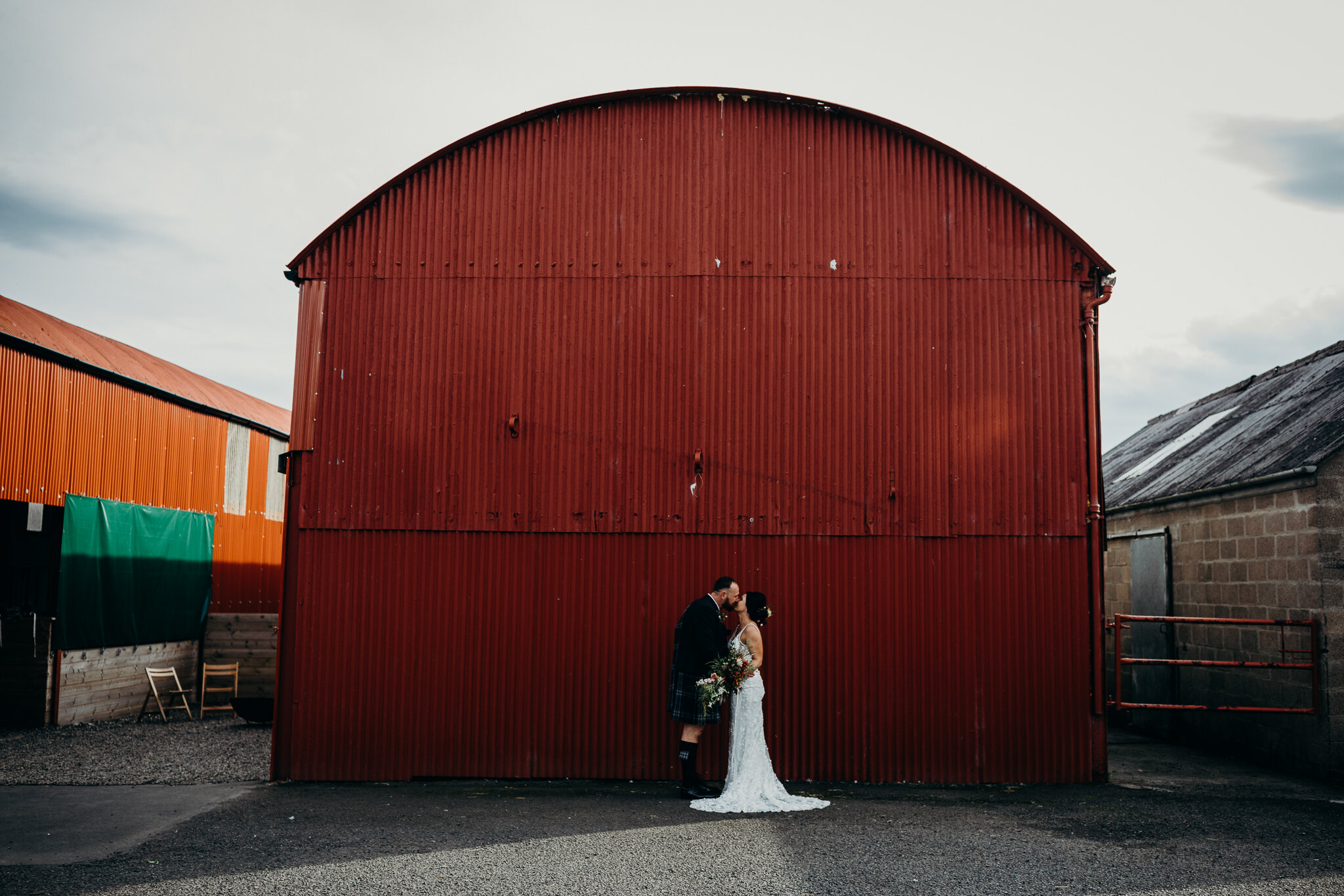 bride and groom kissing outdoors in front of red barn at dalduff farm photographed by wedding photographer ayrshire scotland