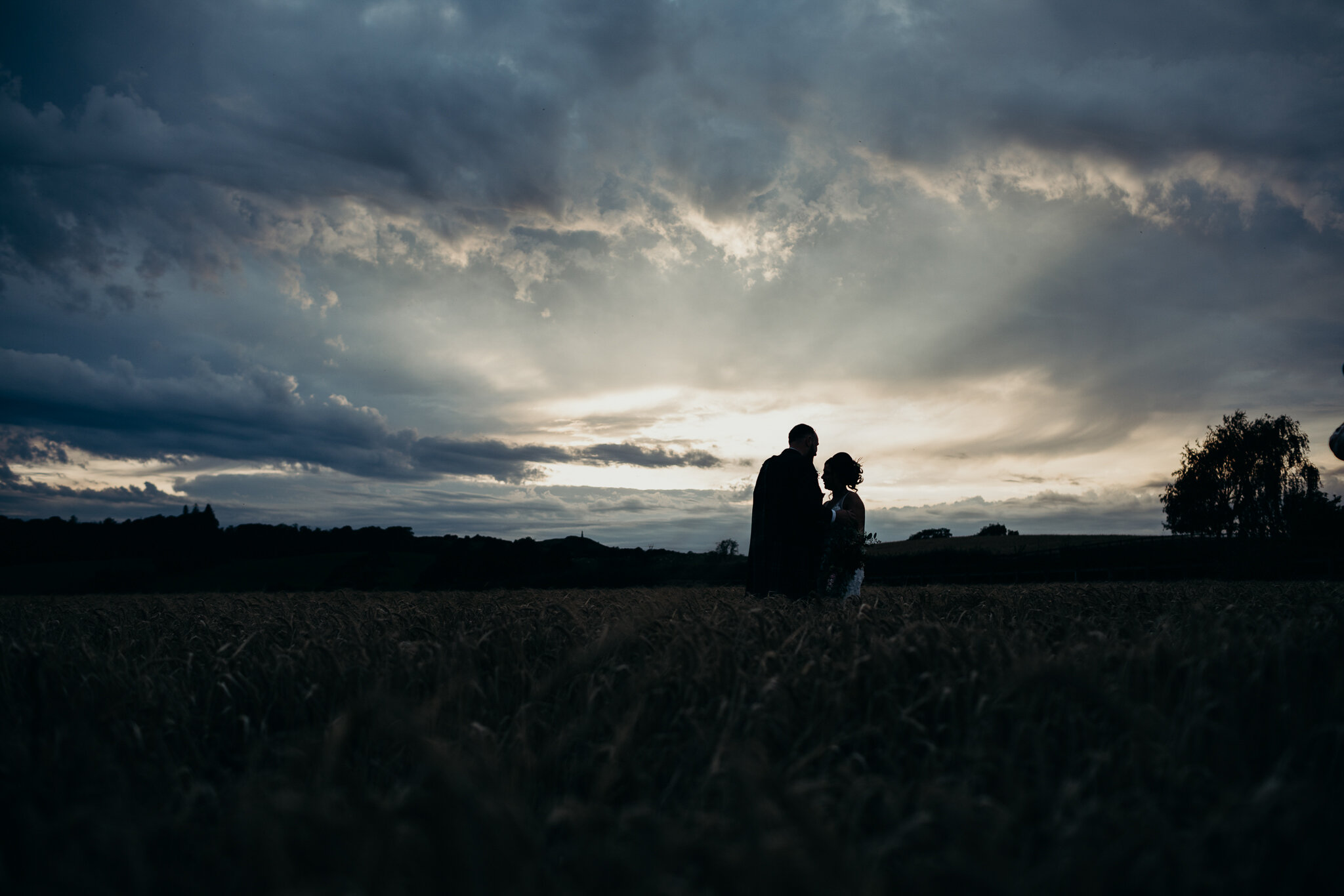 moody image of bride and groom standing outdoors in wheat field at dalduff farm for their barn wedding photographed by wedding photographer ayrshire Scotland