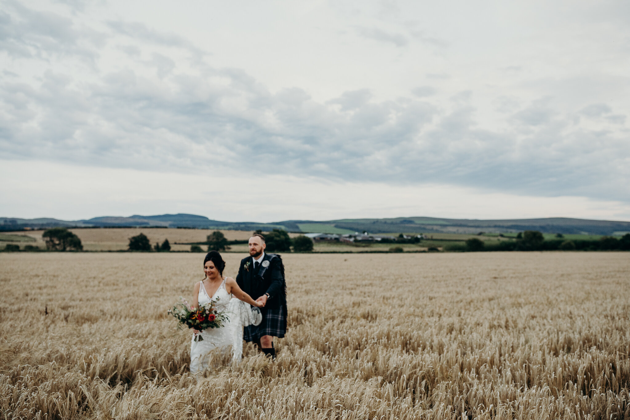 bride and groom walking through wheat field outdoors during barn wedding at dalduff farm photographed by wedding photographer ayrshire Scotland