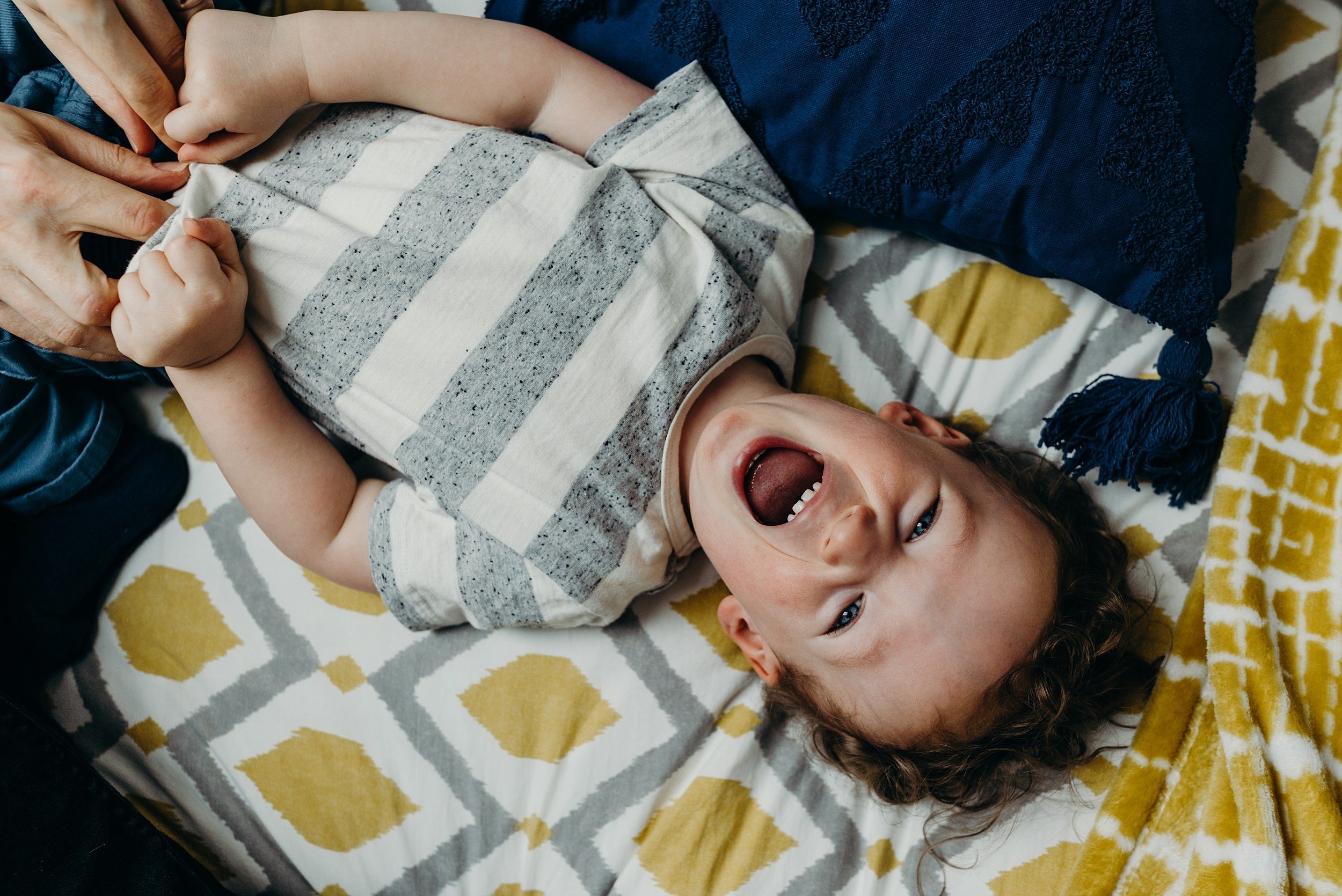 toddler lies on bed and smiles up at the camera during in home baby photography glasgow