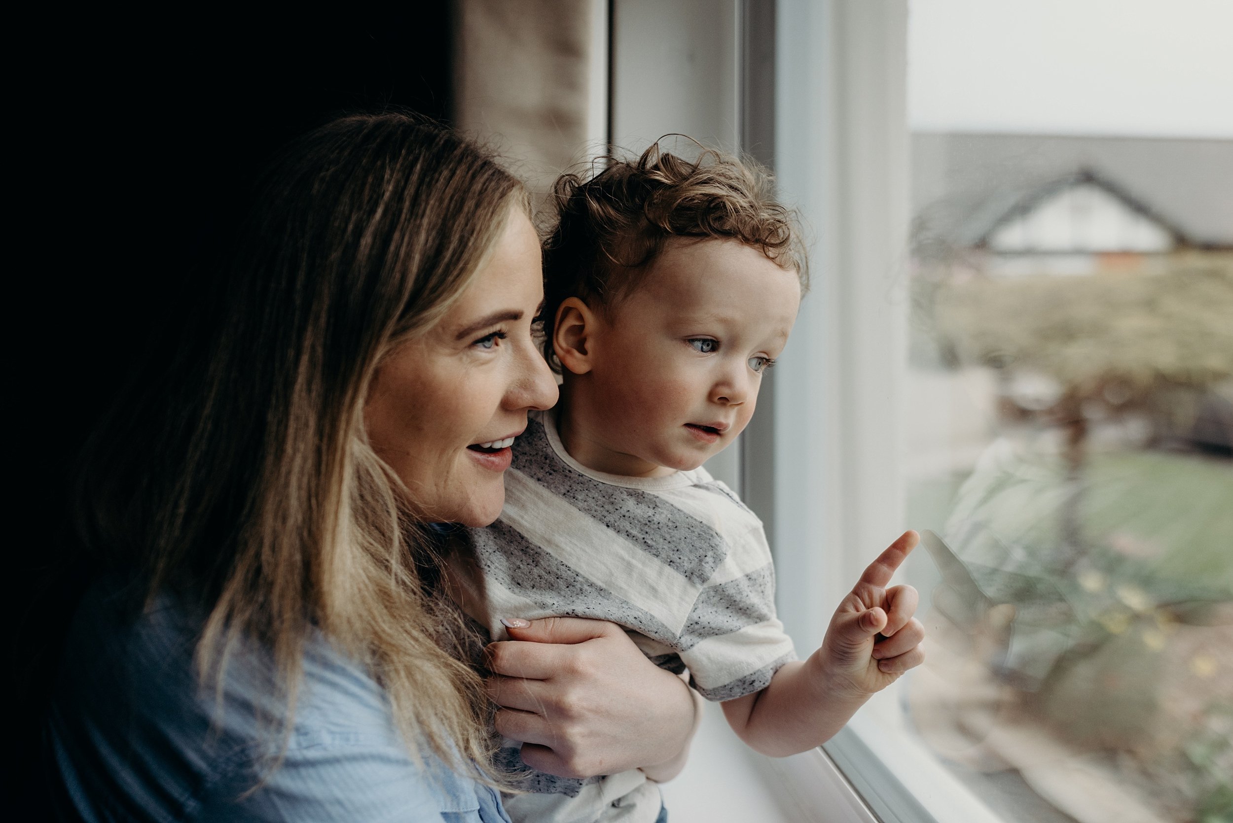 mum and toddler look out window during baby photography glasgow for relaxed in home newborn photo shoots