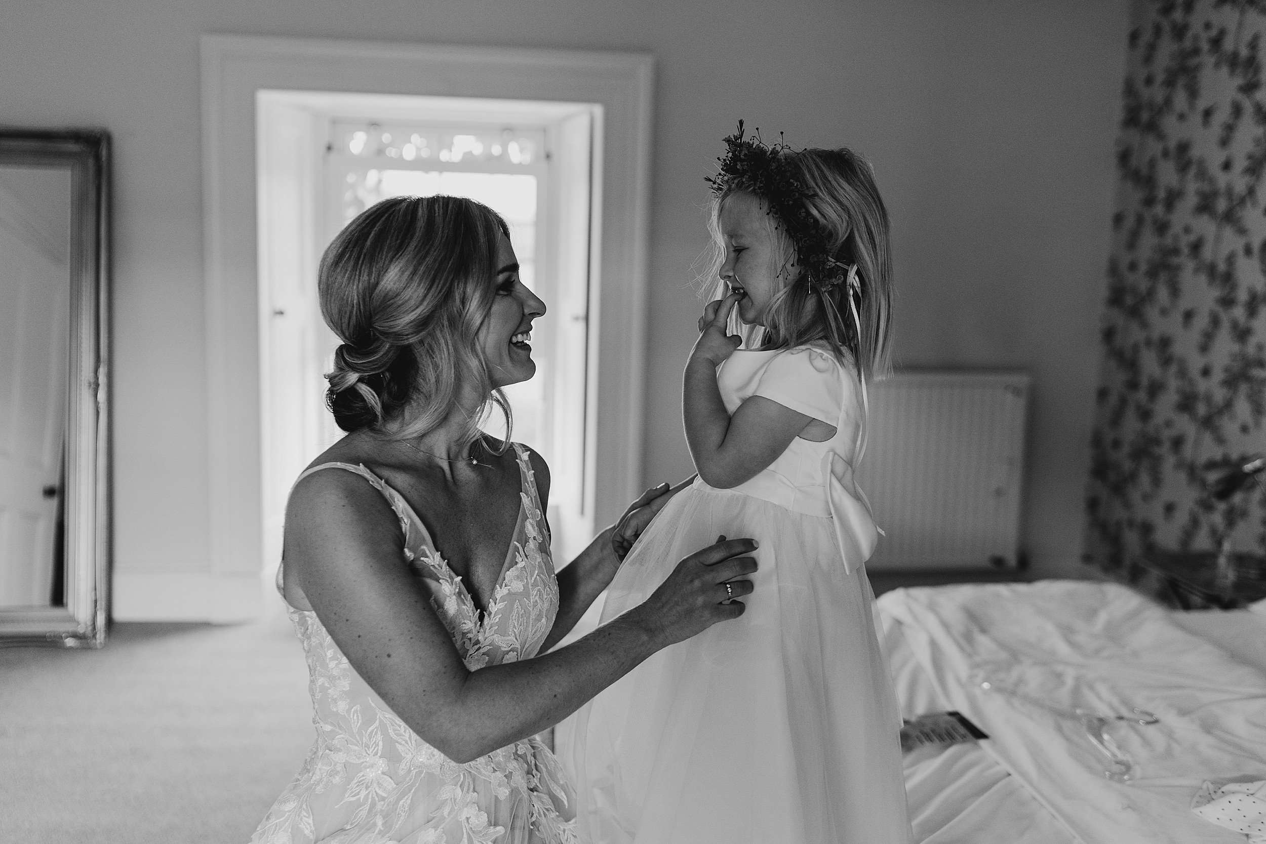 bride and her daughter flower girl smiling at each other whilst getting ready for ceremony at dalduff barn a unique wedding venue scotland