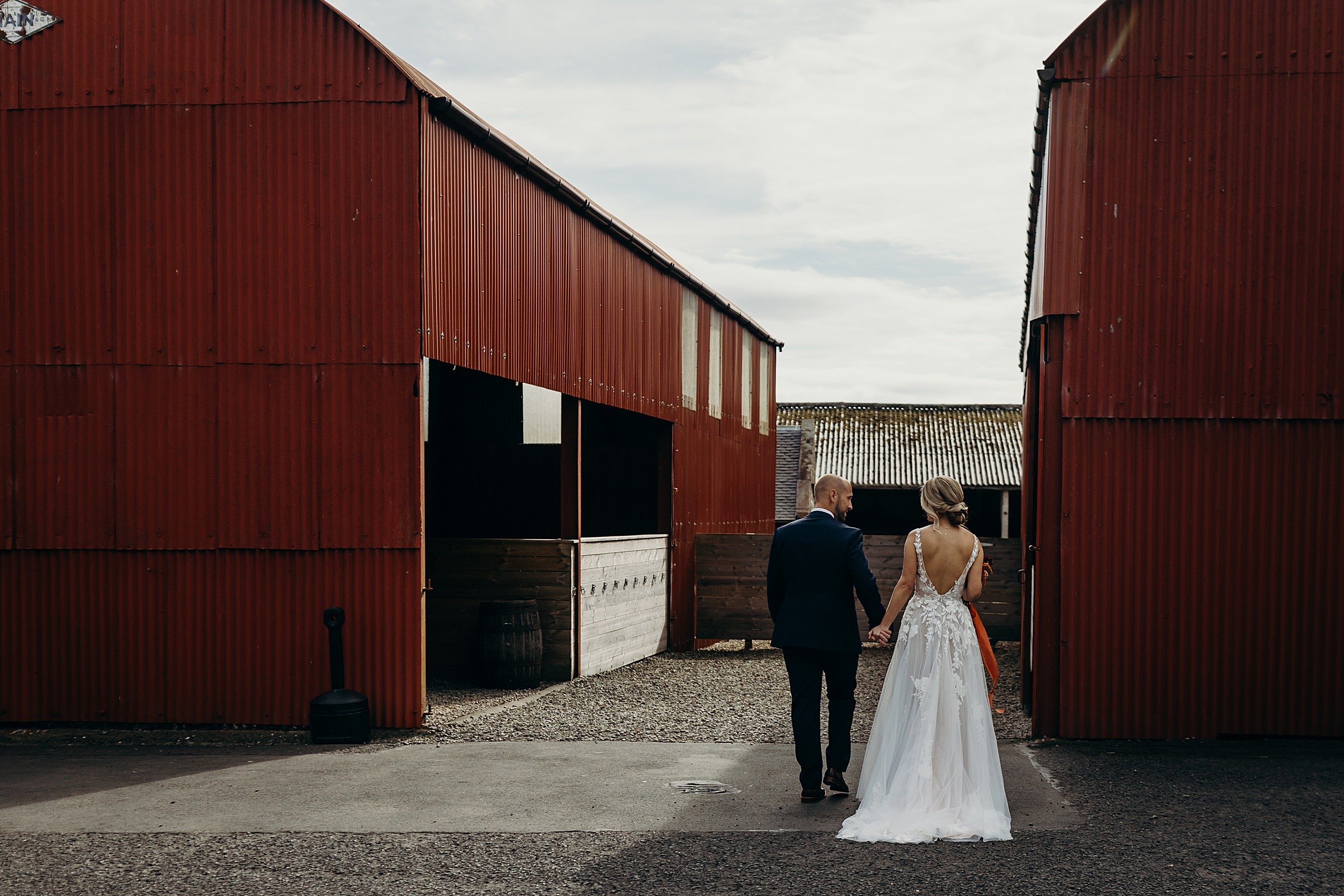 bride and groom holding hands walking in front of red barn wedding venue in scotland at dalduff barn