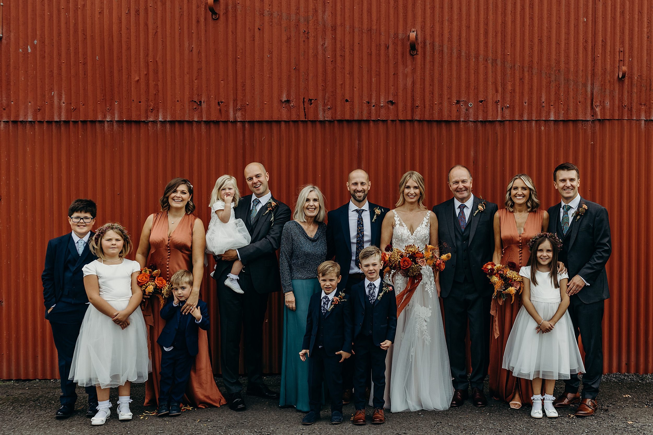 dalduff farm wedding photos showing bride and groom with family standing in front of red barn at dalduff barn a quirky wedding venue in scotland