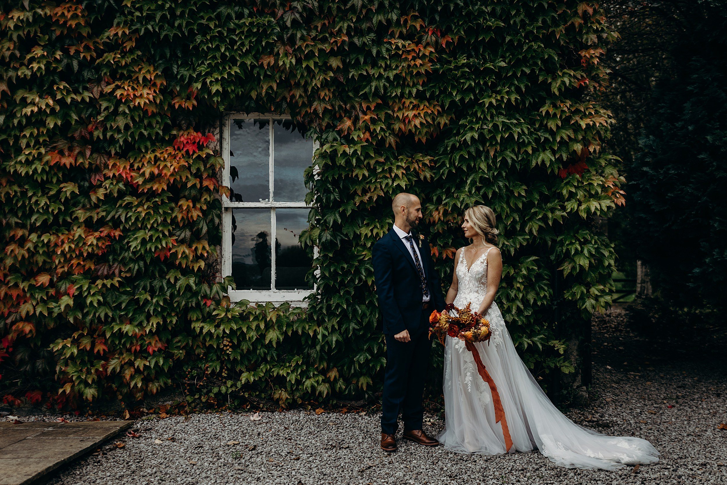 bride and groom looking at each other standing in front of green ivy wall outside farmhouse at dalduff barn shown in dalduff farm wedding photos