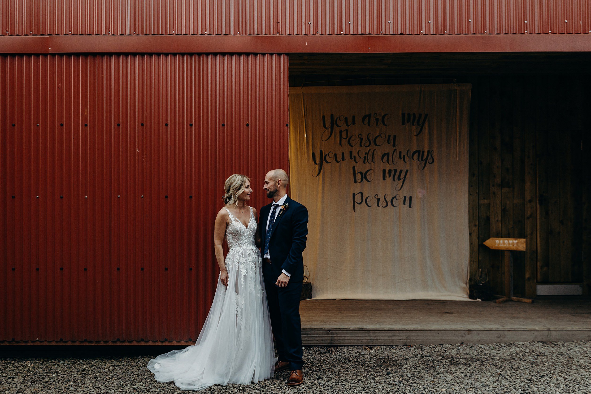 bride and groom standing in front of wedding barn with calligraphy banner at dalduff barn
