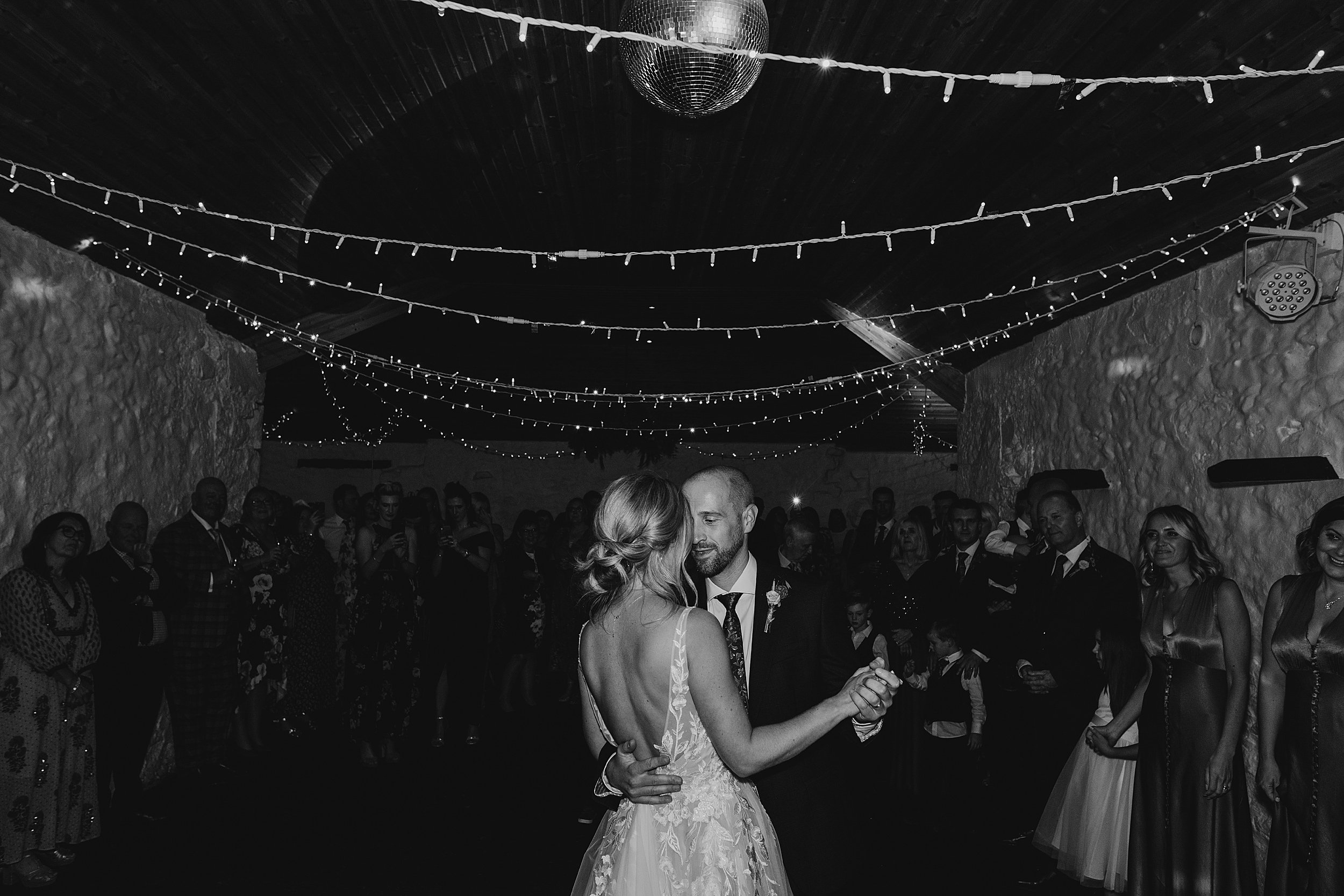 bride and groom during first dance inside dalduff barn under fairy lights and disco ball as shown in dalduff farm wedding photos