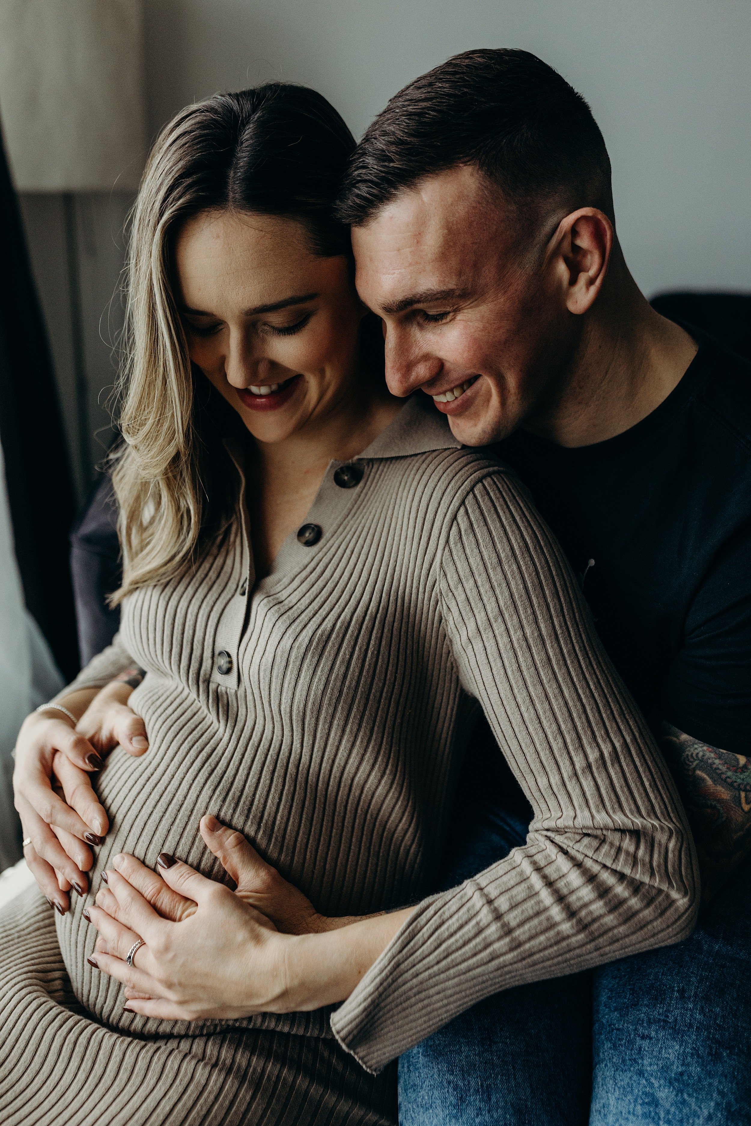 mum to be and dad to be cuddling smiling and holding baby bump during pregnancy photo session by maternity photographer glasgow