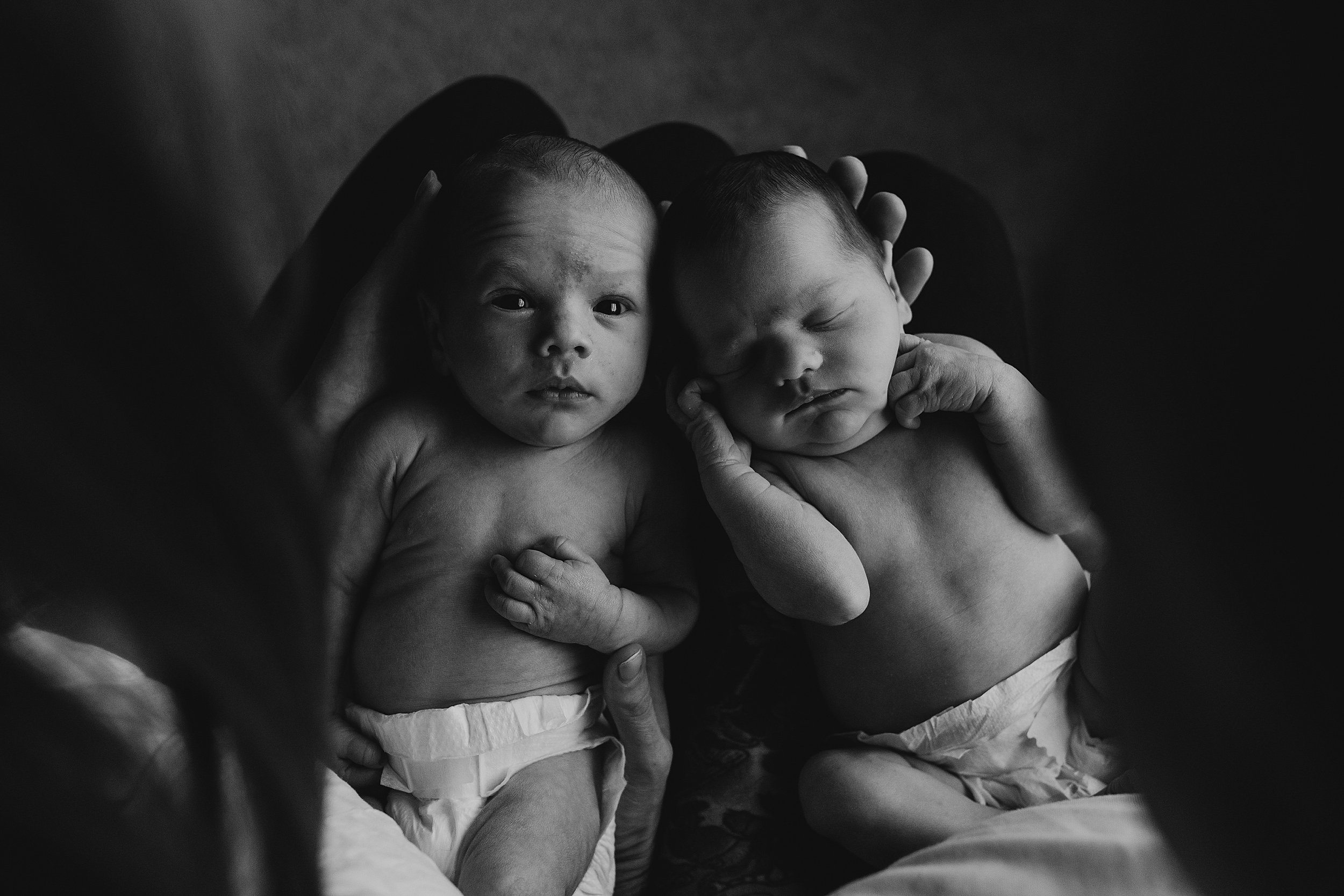 newborn twin babies being held in their parents arms with one baby looking at the camera in a black and white photo session by maternity photographer glasgow