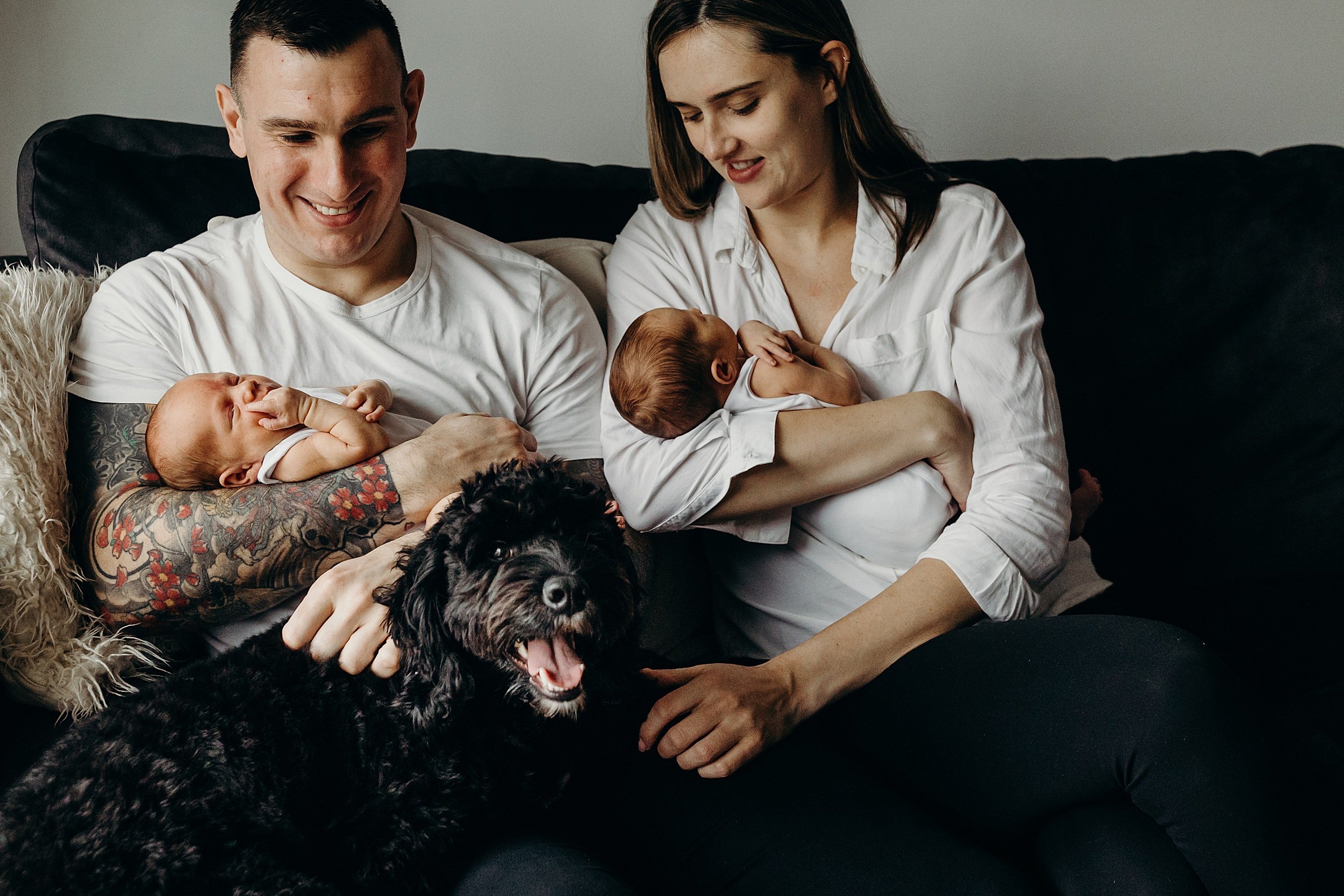 mum and dad sitting on sofa holding their newborn twin babies with their dog during an at home newborn photo session glasgow