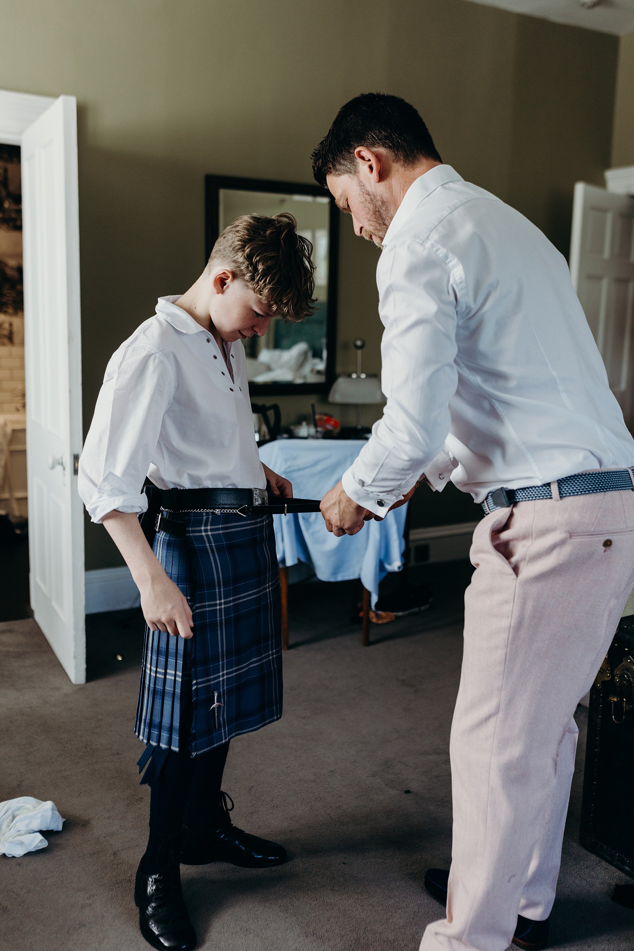 groom helping son put on his kilt in room in one Devonshire gardens for the bothy glasgow wedding