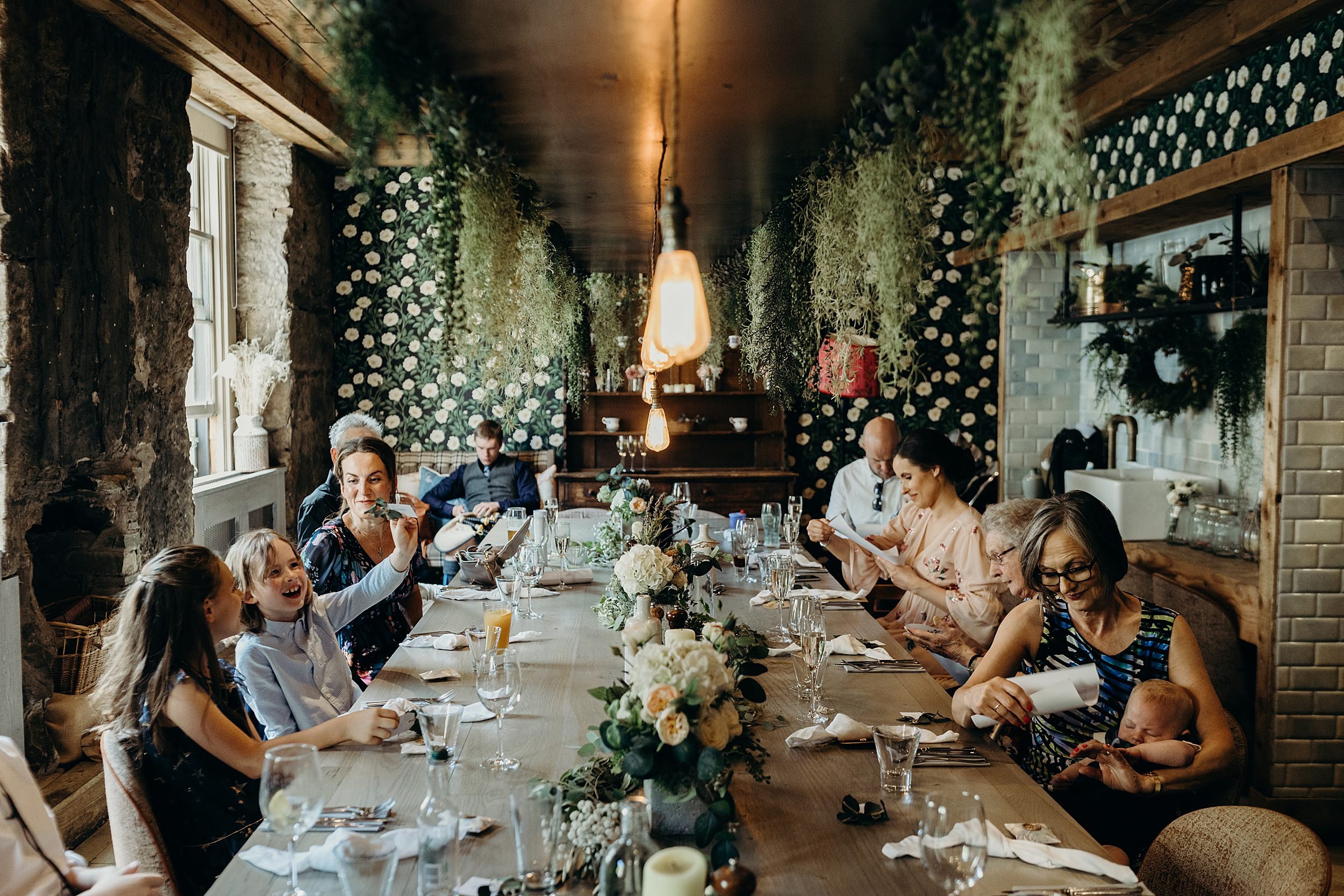 wedding guests seated at table during small wedding at the bothy glasgow with hanging green foliage and pendant lights