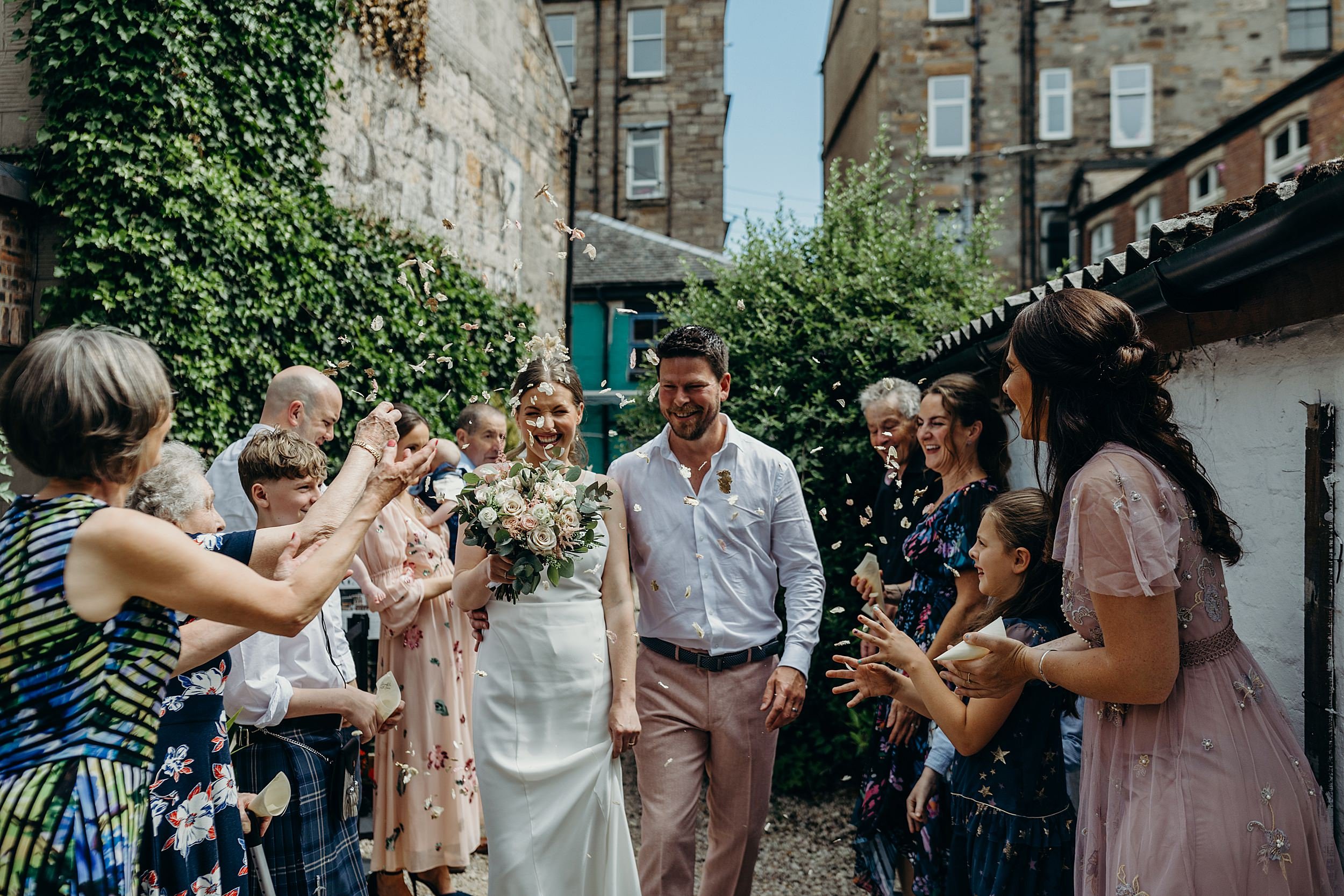bride and groom smiling and walking under colourful confetti throw after their mini wedding ceremony at the bothy glasgow wedding