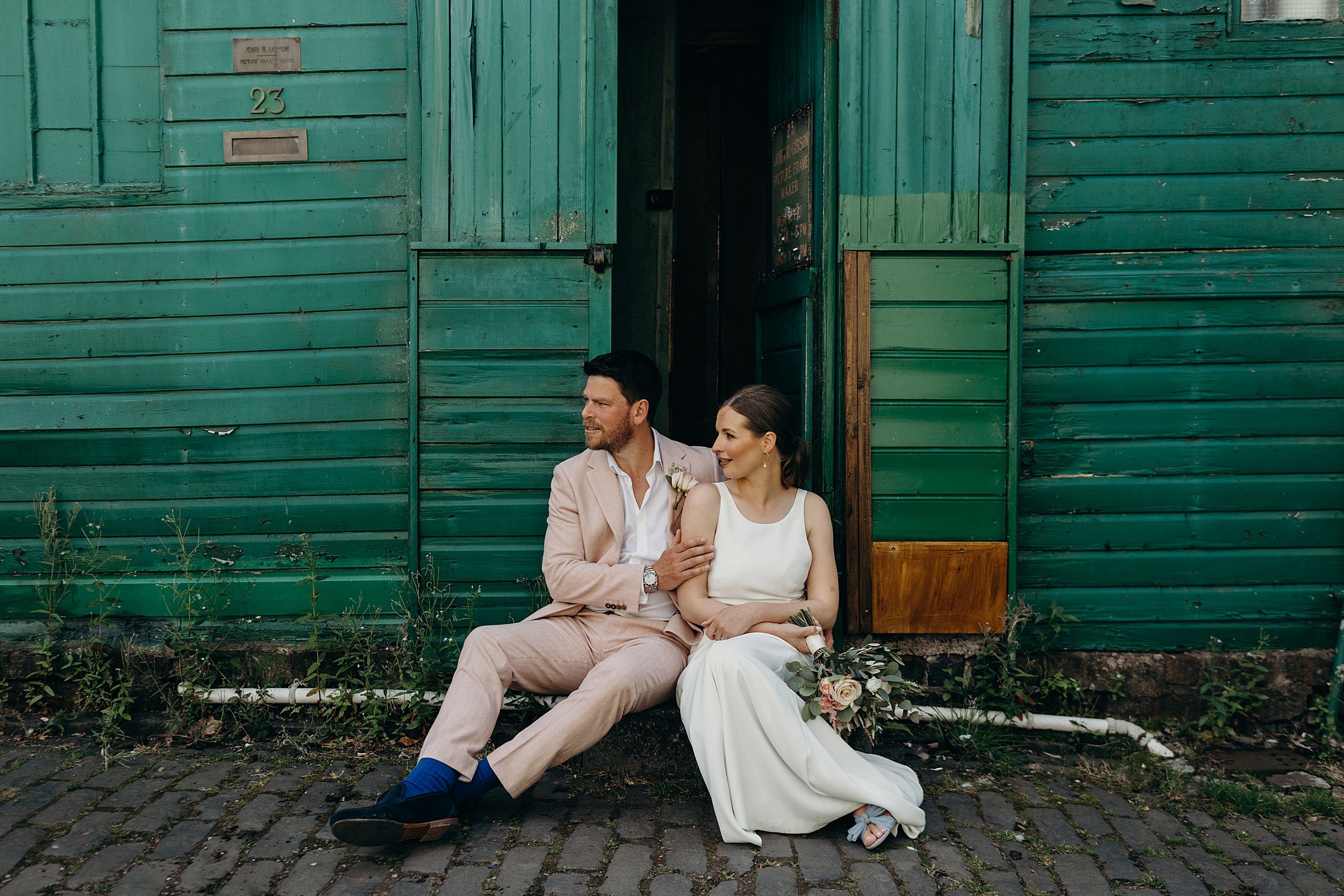 bride and groom sitting on steps outside green wooden building after their ceremony at the bothy glasgow wedding