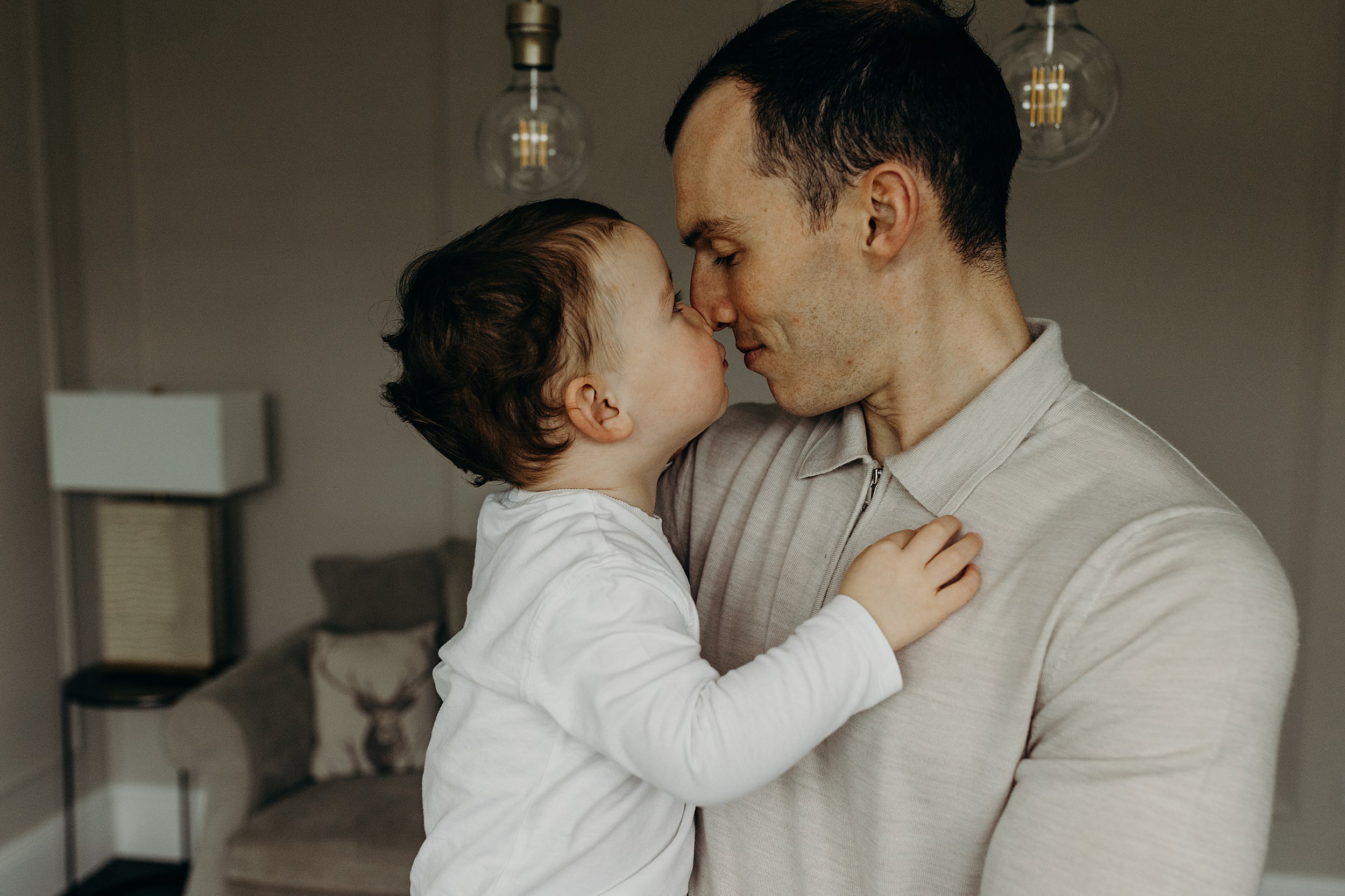 father holds his toddler boy they are nose to nose in a living room during a family photographer glasgow scotland photoshoot