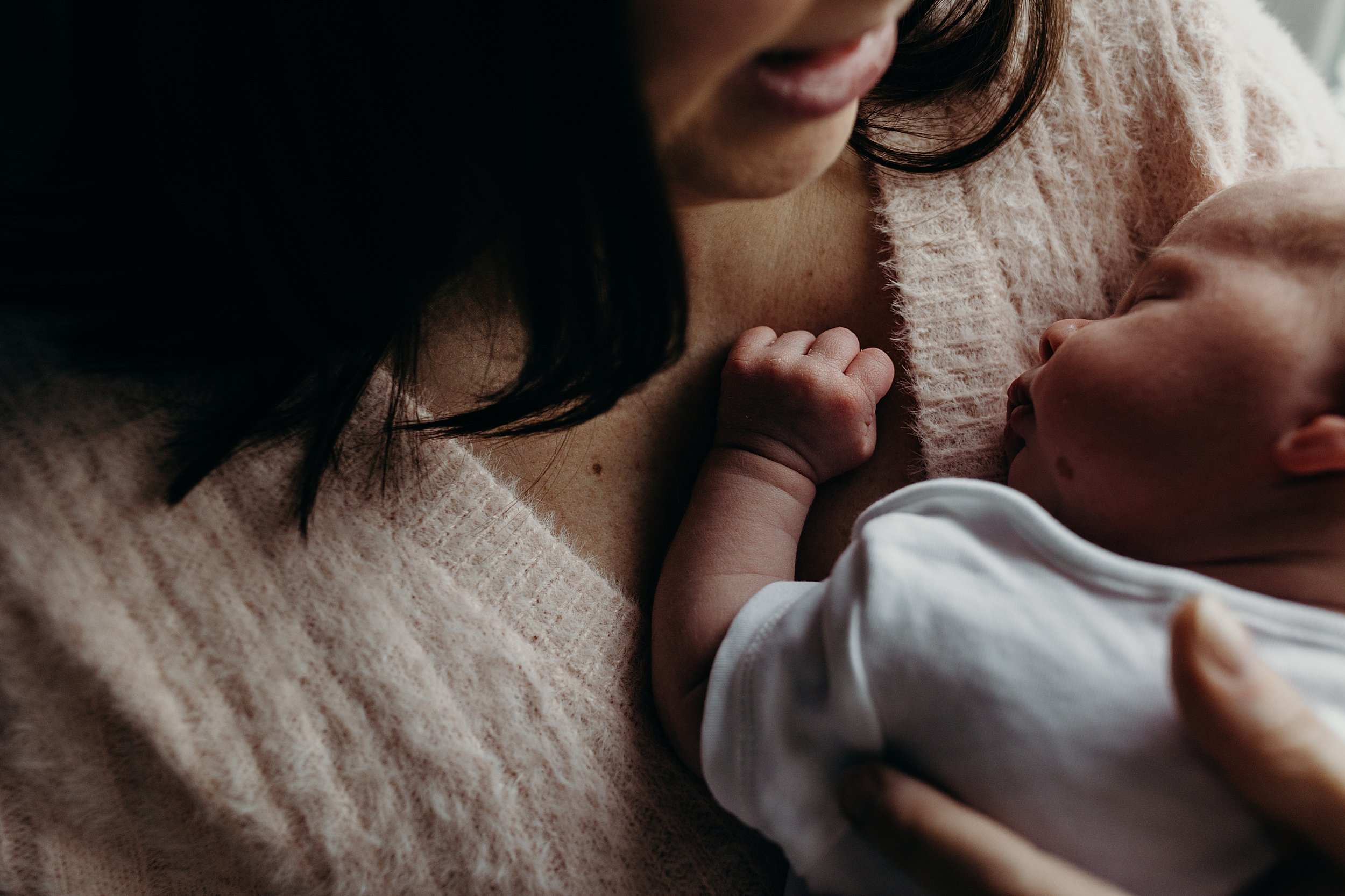 mother wearing a pink sweater holds her sleeping baby daughter against her chest during newborn photoshoot glasgow scotland