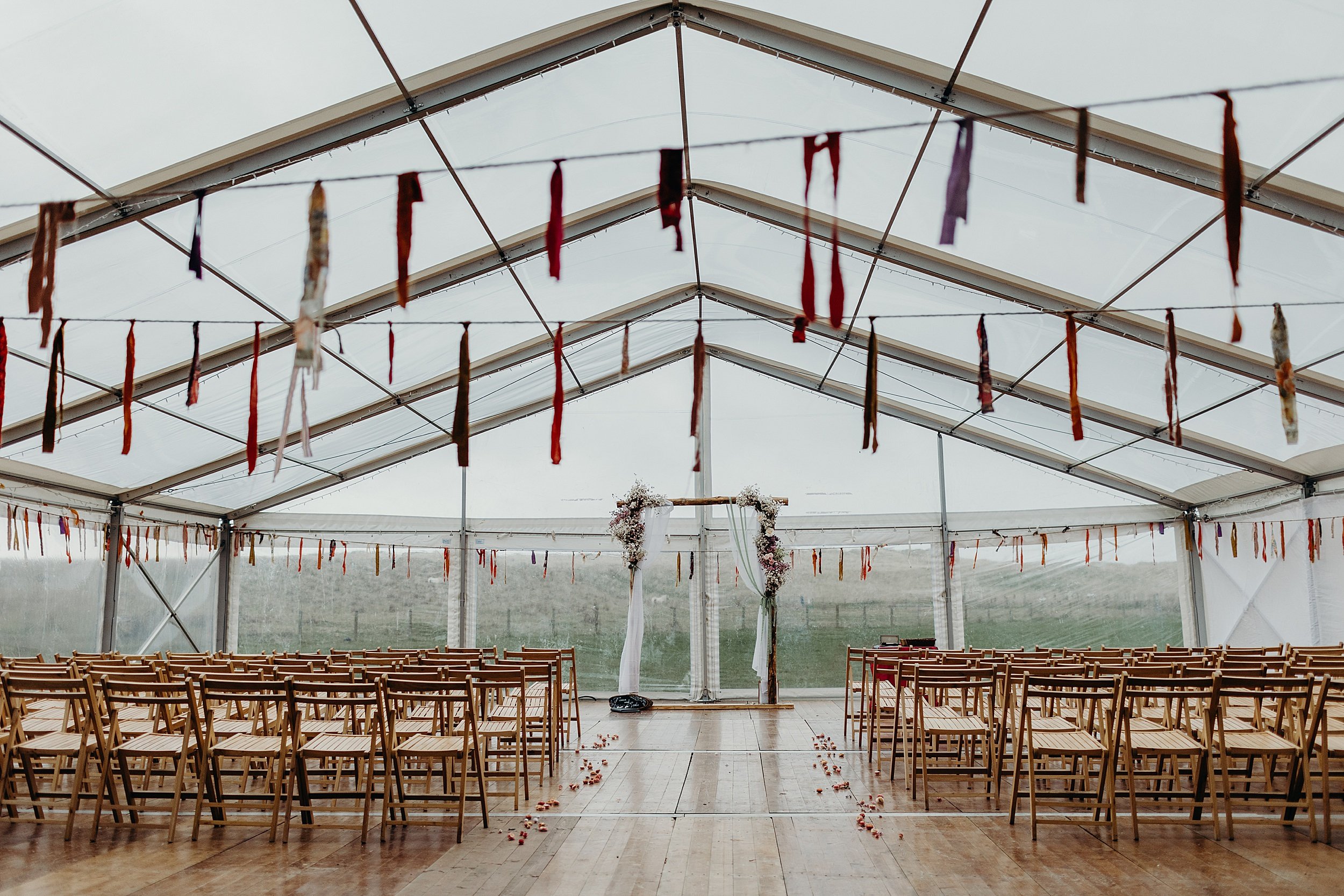 interior inside view of a marquee set up for a wedding with wooden chairs and ribbon garlands at harvest moon wedding venue in east lothian in scotland