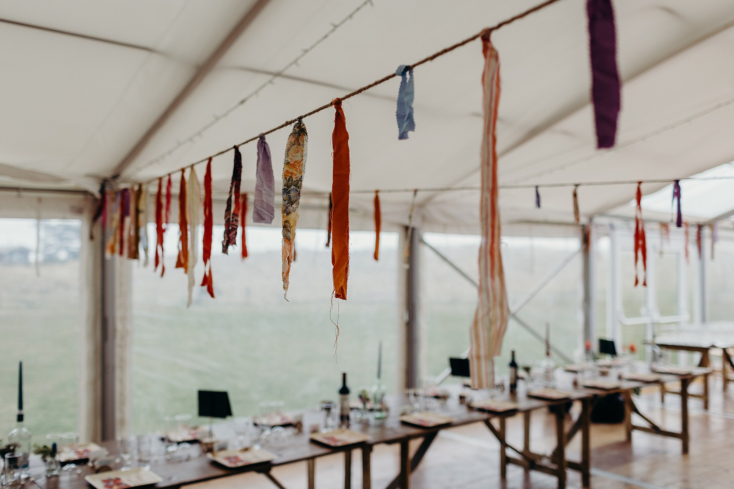 tables set for dinner with ribbon garlands hanging above inside a marquee at harvest moon wedding venue in dunbar scotland