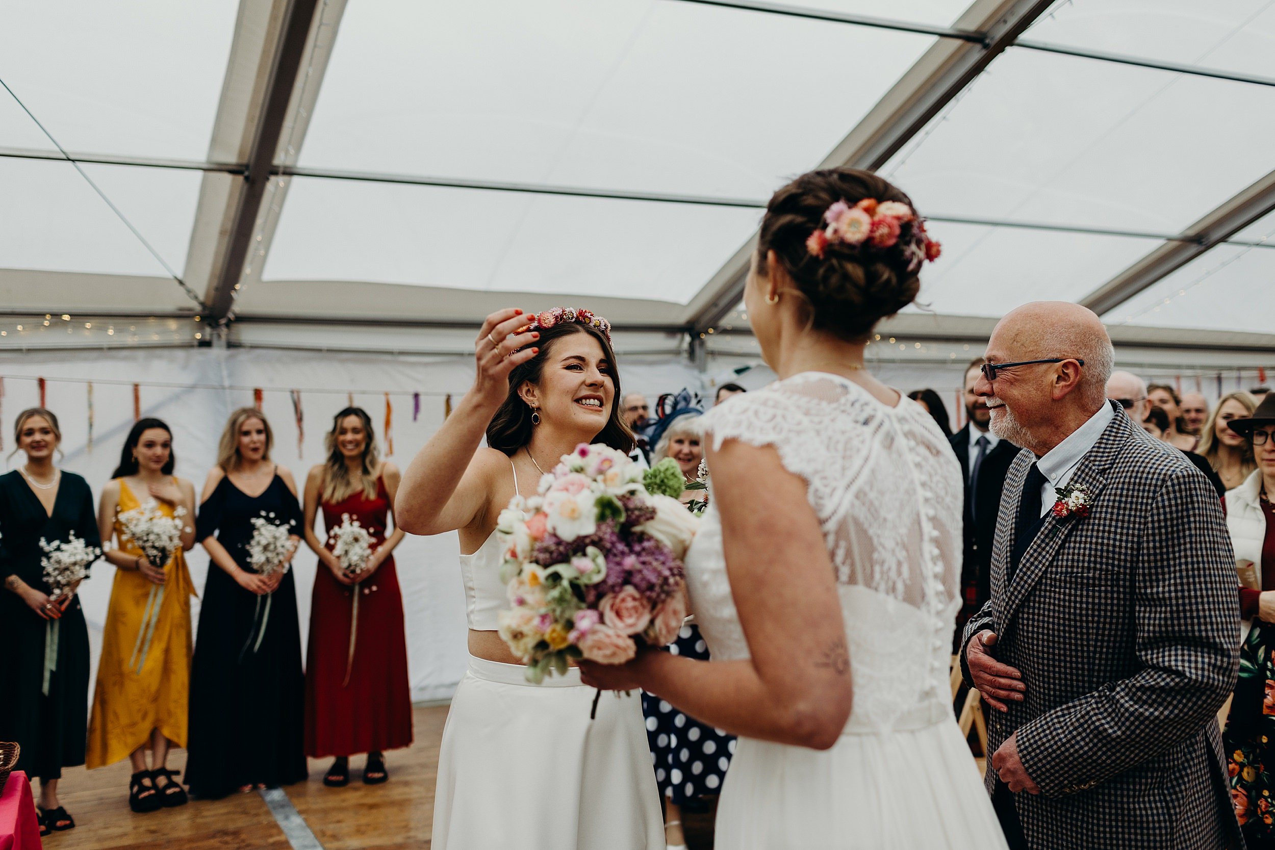the two brides greet each other as bridesmaids and guests look on before their harvest moon wedding in dunbar in scotland