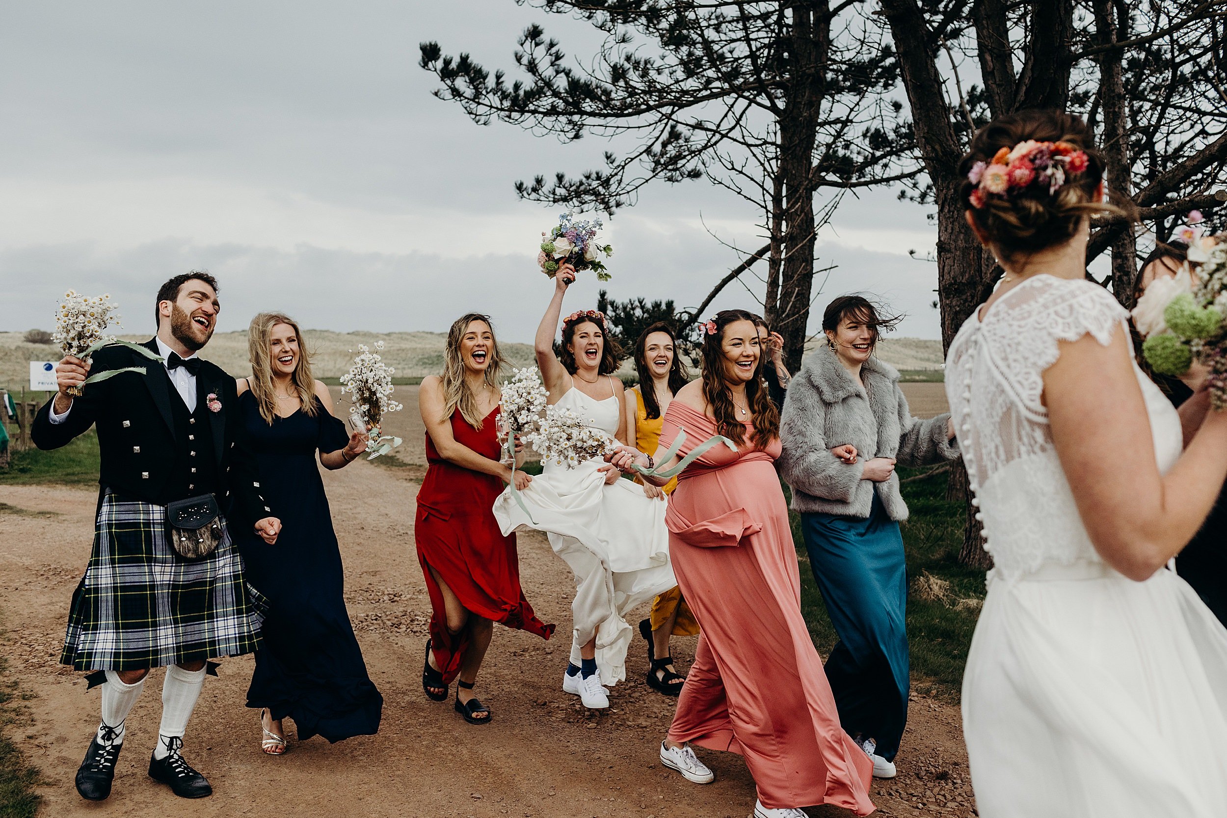 two brides and their guests walk along a country path following their harvest moon wedding in dunbar scotland
