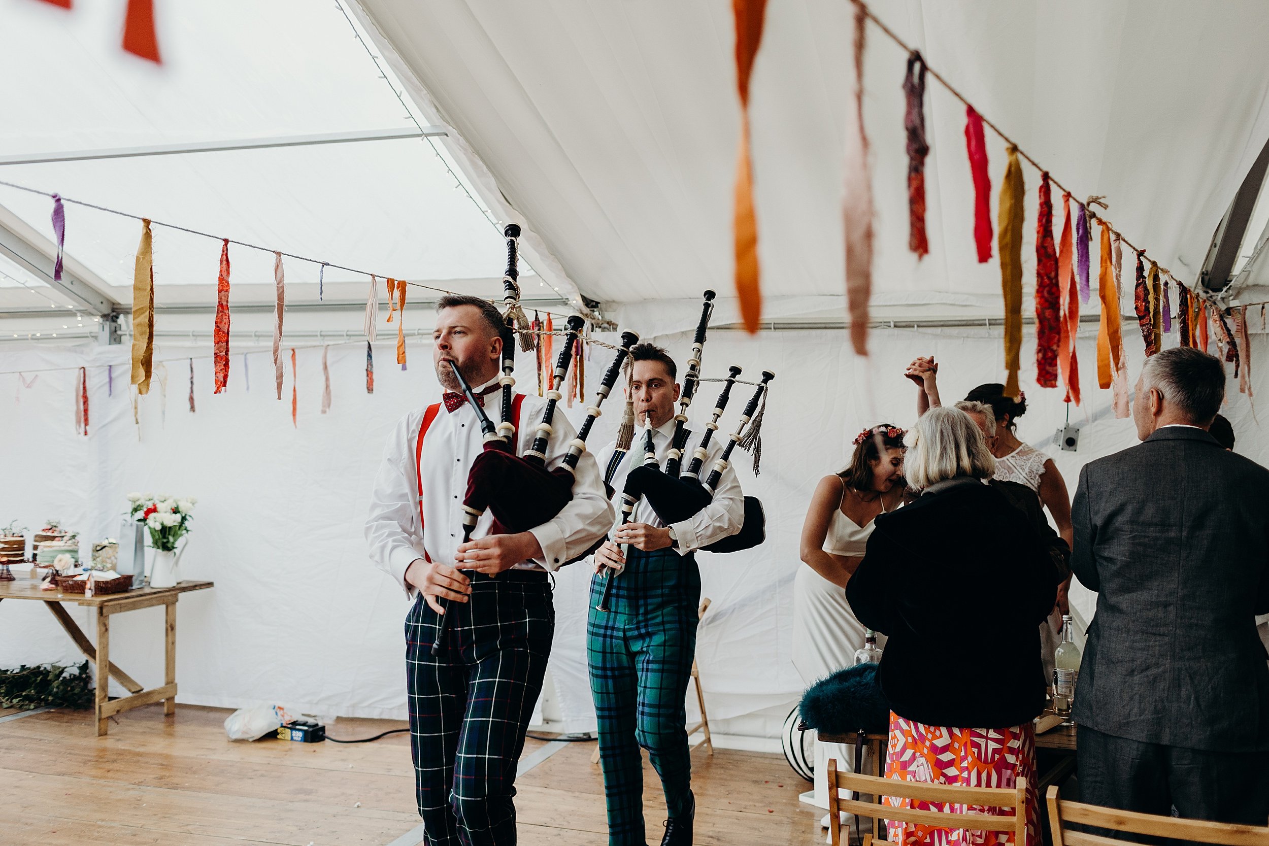 two pipers lead the two brides into the marquee hung with ribbon garlands for their harvest moon wedding dinner