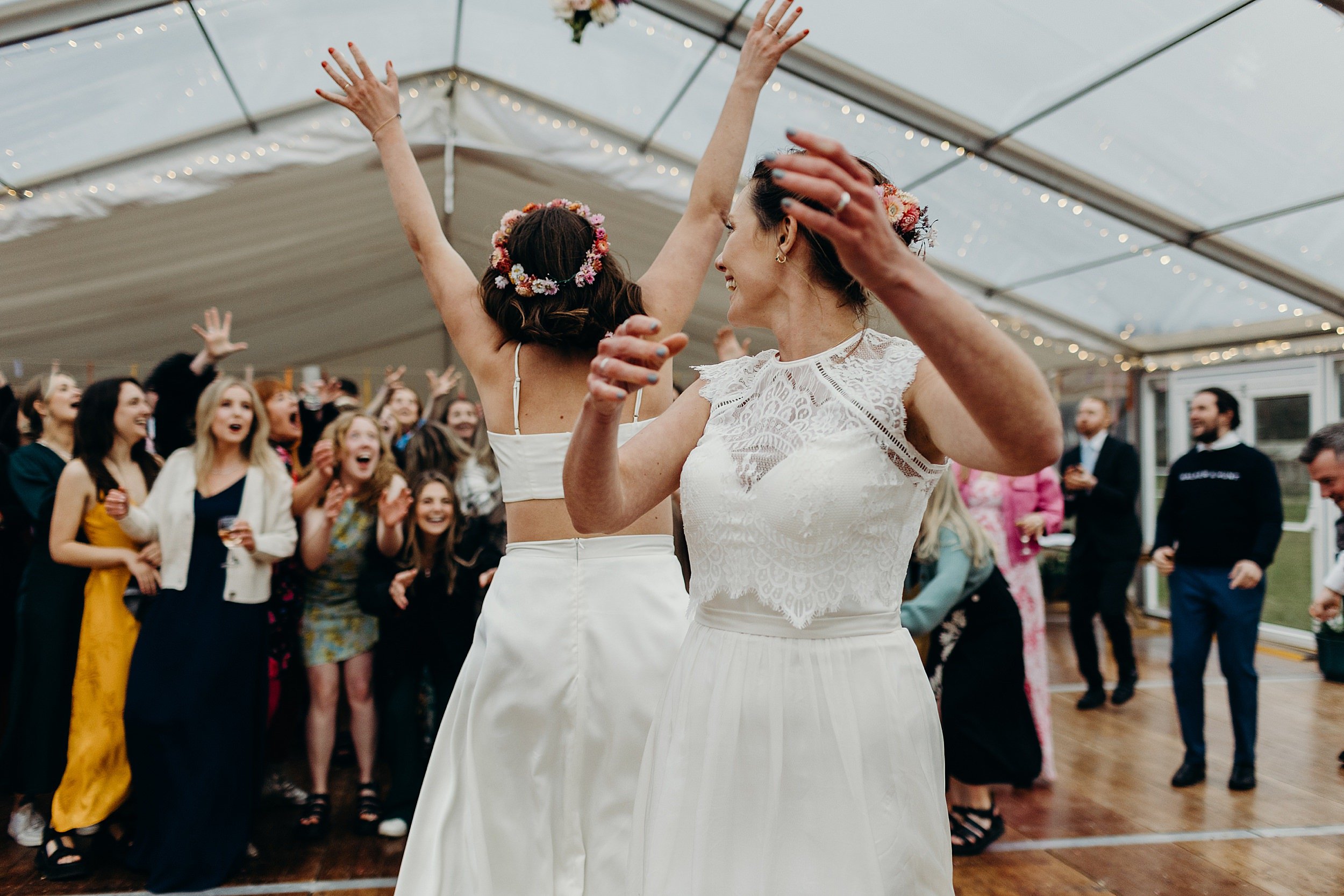 a bride tosses her bouquet into the crowd of guests inside a white marquee at harvest moon wedding venue in East Lothian in Scotland