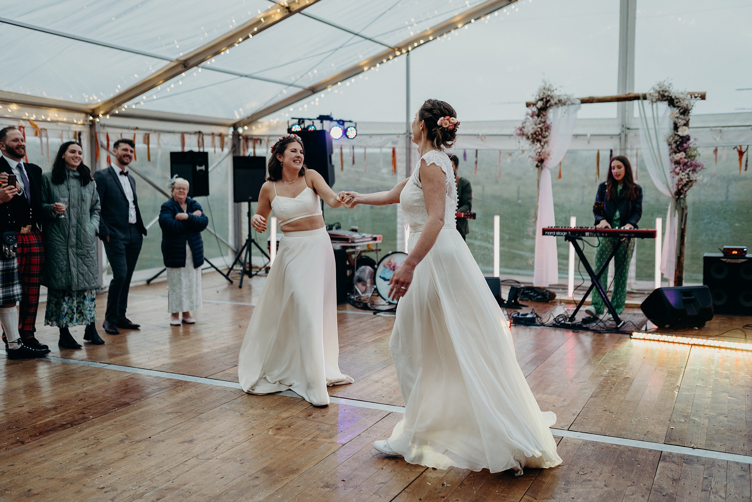 the two brides dance their first dance in a white marquee at harvest moon wedding venue in dunbar scotland