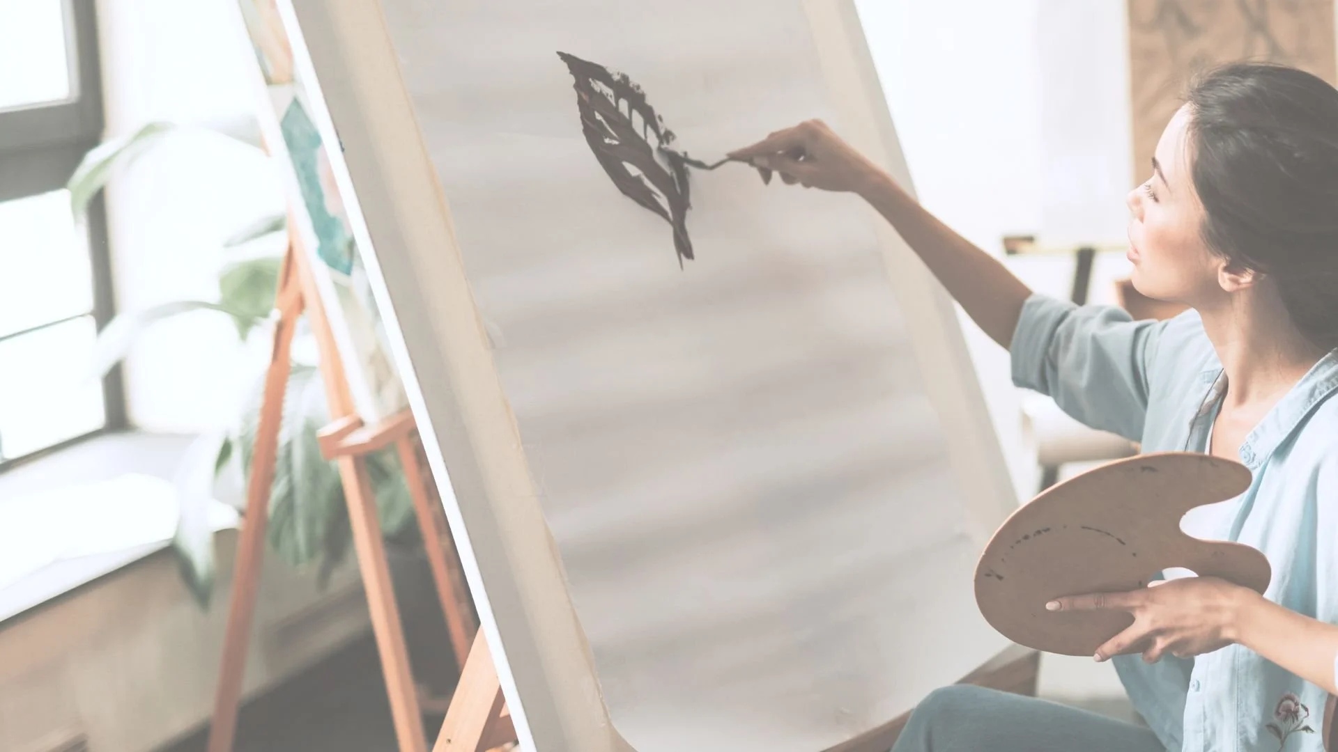 A woman sitting on a wooden floor, painting abstract blue wave-like patterns on canvases with watercolor paint. Several finished paintings and art supplies are nearby.