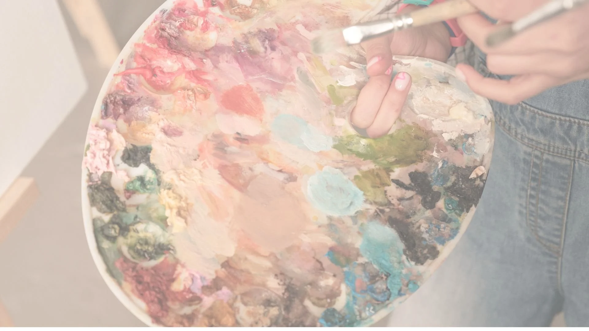 Person coloring a floral illustration on paper with watercolor paints and brushes, surrounded by painting supplies, water glass, and scribbled sketches.