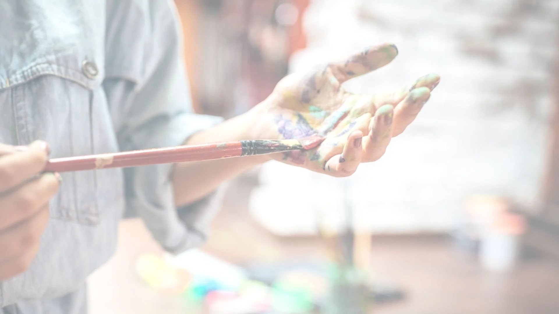 A woman painting with watercolors at a table, surrounded by art supplies and papers.