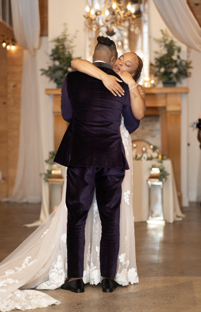 Bride and groom embrace in elegant indoor wedding space with soft light, chandeliers, and draping.
