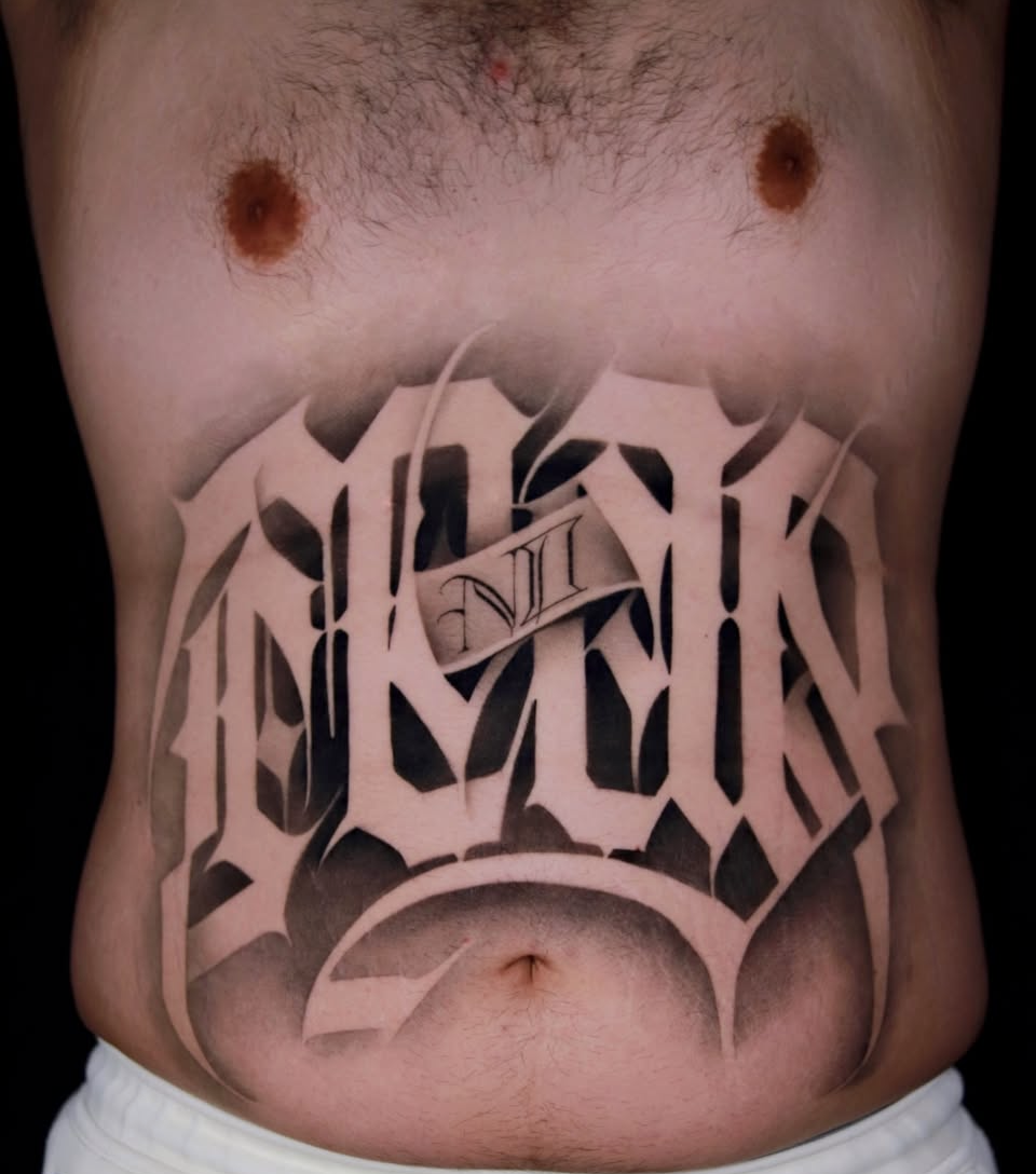 Bold black and grey custom script tattoo across the stomach, featuring clean lettering, smooth shading, and striking contrast. Custom tattoo work by Bauz at Motor City Tattoo Studio.