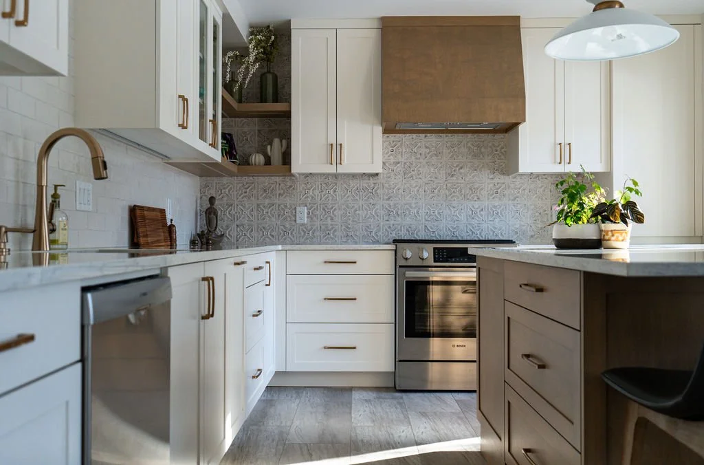 Modern kitchen with white cabinetry, stainless steel appliances, a patterned backsplash, and a kitchen island with potted plants.