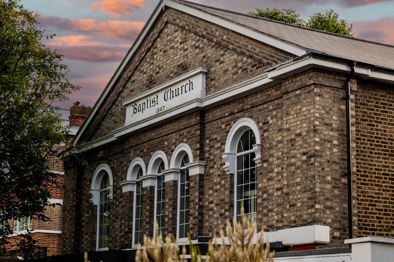 The brick facade and arched windows of New Park Road Baptist Church beneath an evening sky.