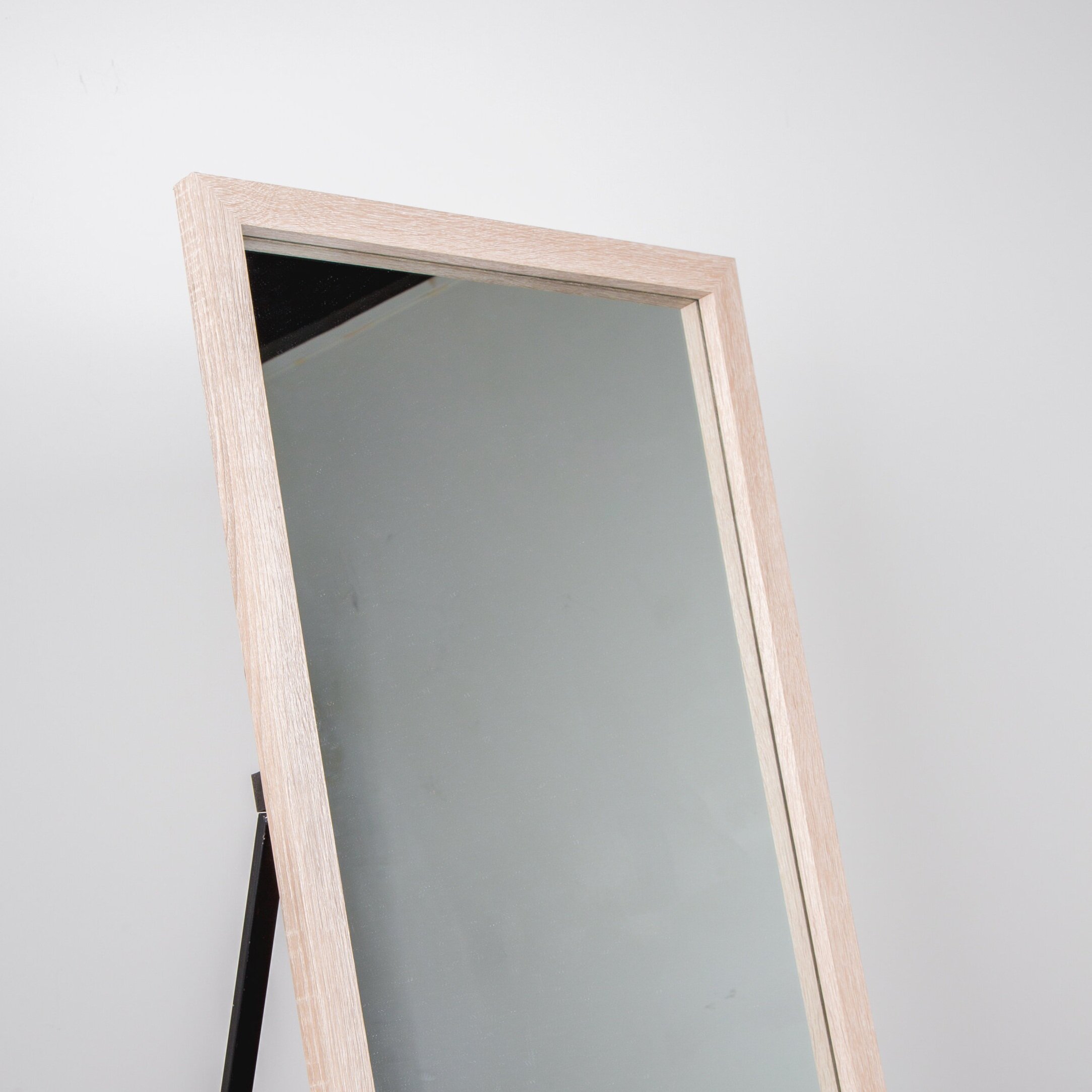 free standing mirror with wooden frame next to white wall