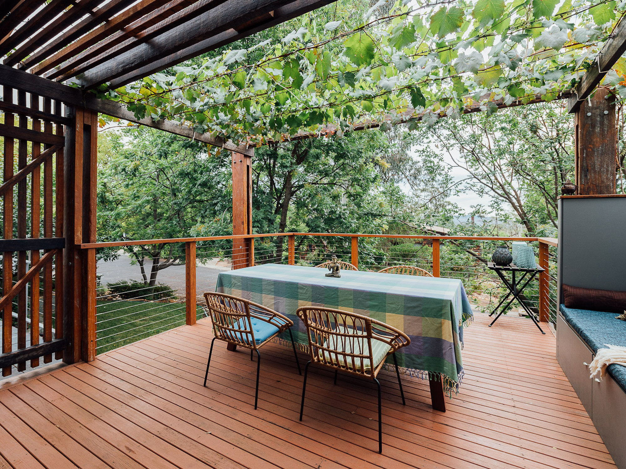A lovely timber deck with a table and chairs in the middle, surrounded with green plant leaves