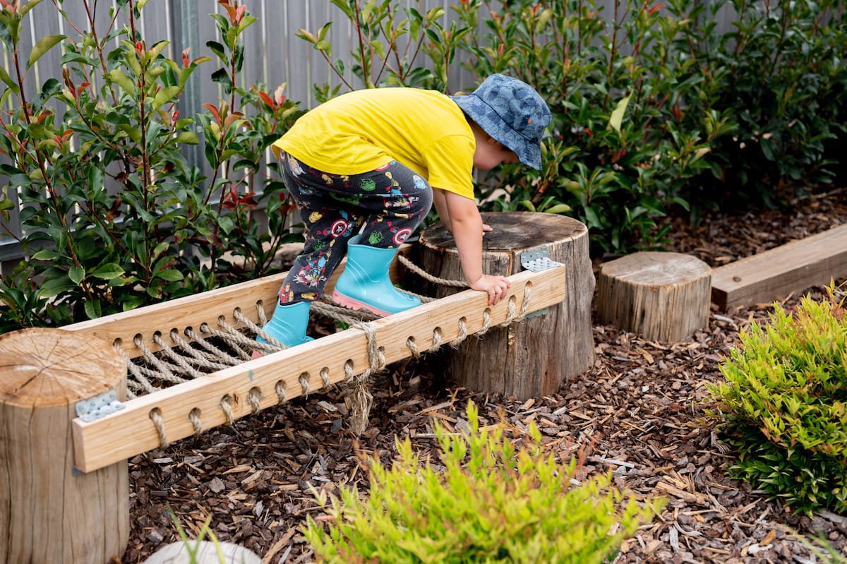 A kid enjoying the obstacle course in their garden made from round recycled timber posts