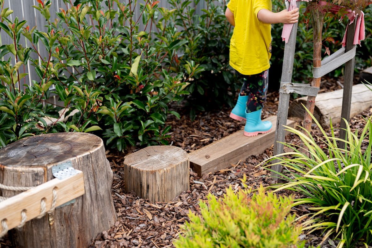 A kid enjoying the obstacle course in their garden made from round recycled timber posts