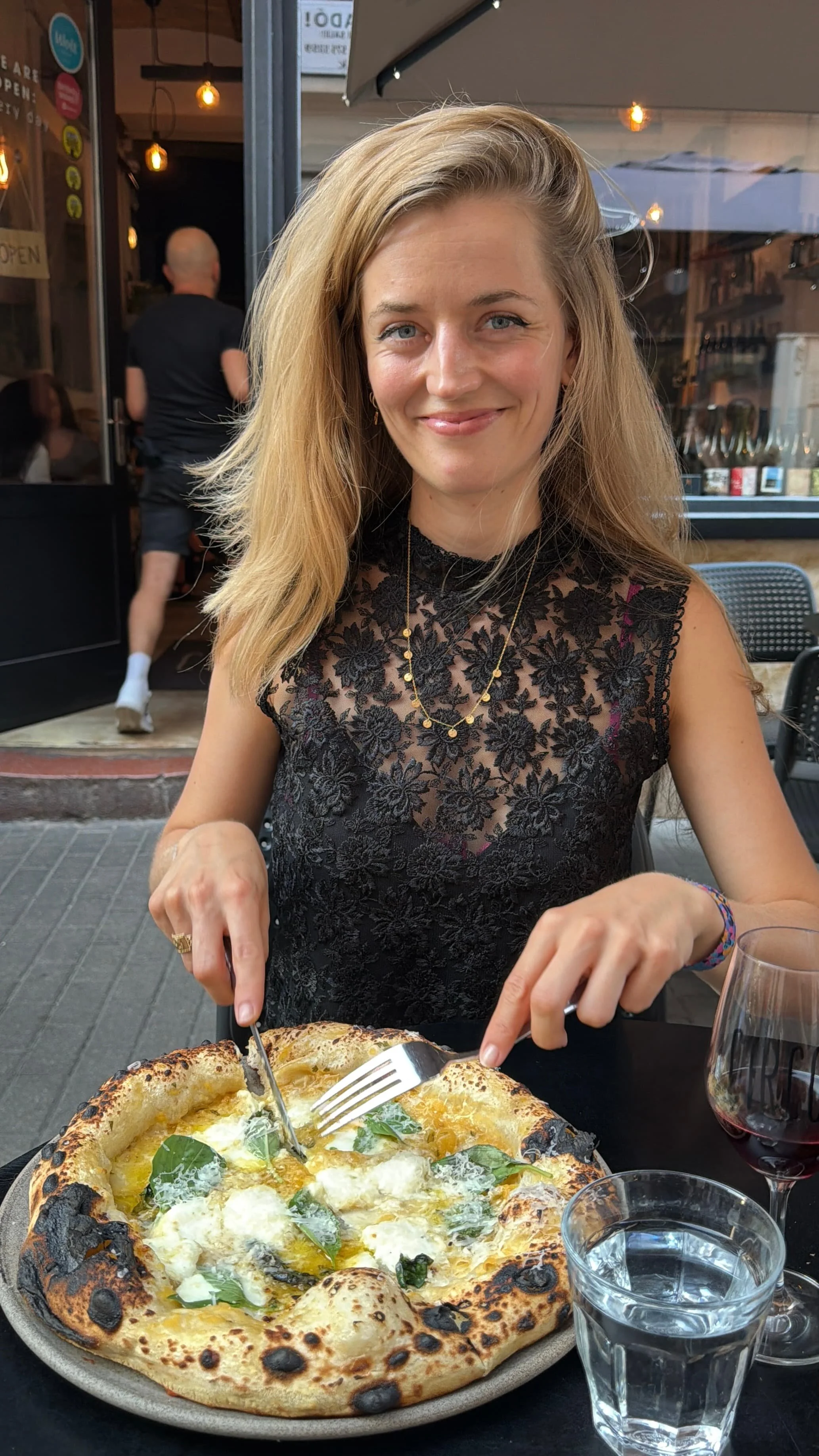 A girl eating pizza with a glass of wine next to her
