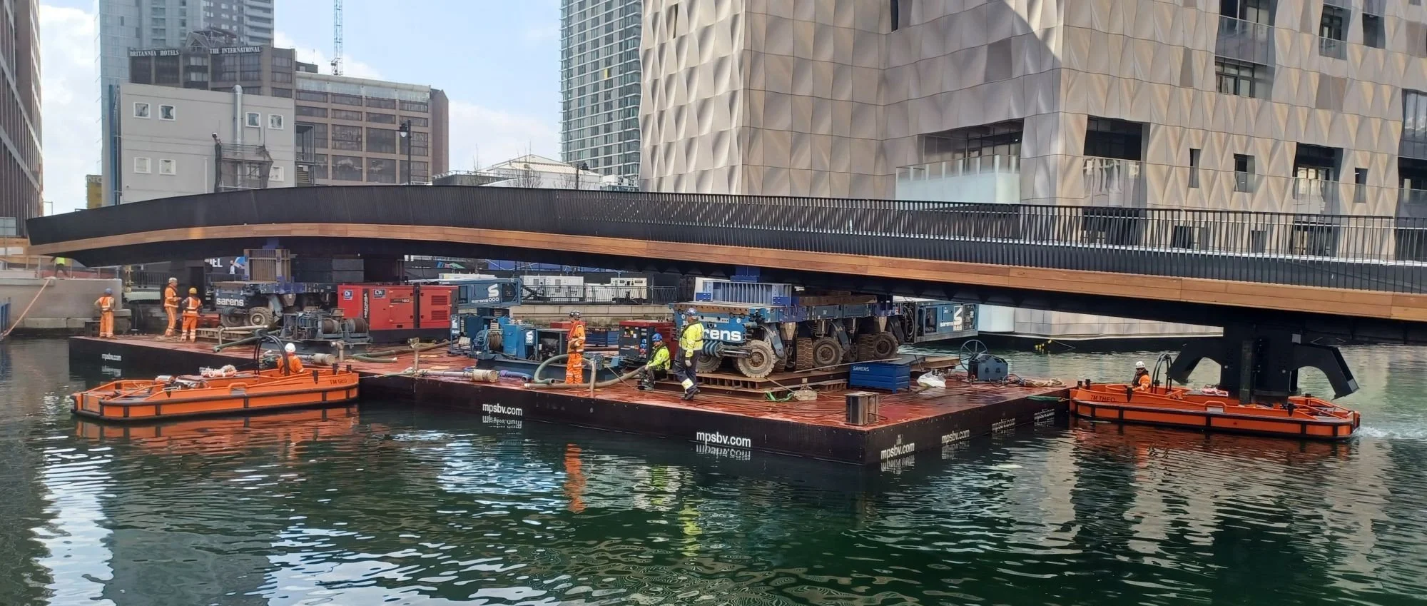 Multiple work boats moving barge to install a 60m bridge in Canary Wharf middle dock