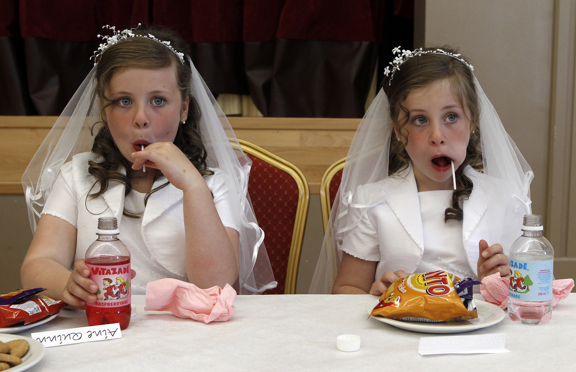 Twins, Aine(left) and Emer Quinn(right) eat sweets in the local parish hall after making their First Holy Communion in St Mary's Roman Catholic Church, Cushendall, 2010.