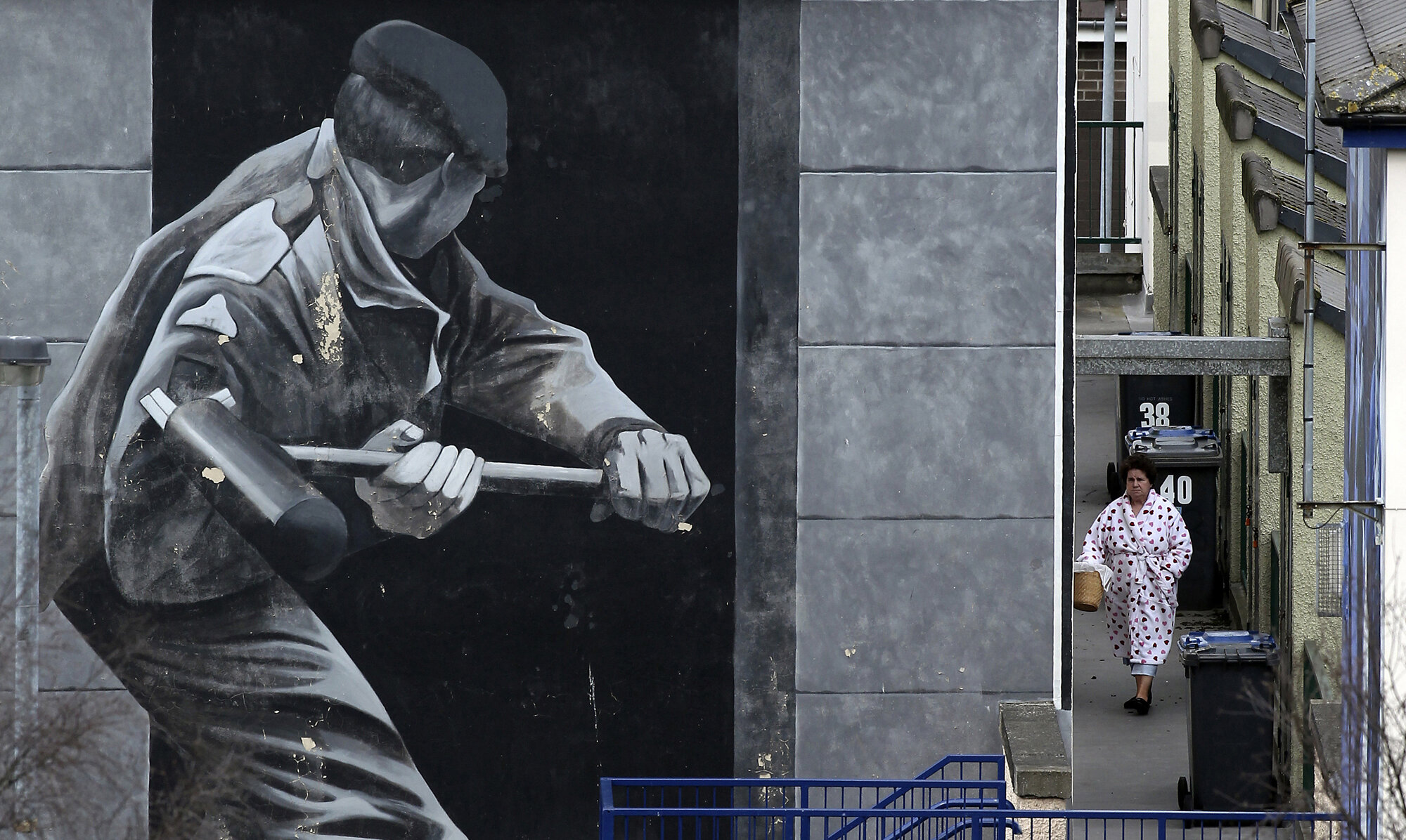 A woman takes out her garbage beside a mural depicting a British soldier knocking down the door of a house with a sledge hammer in Derry, 2010.