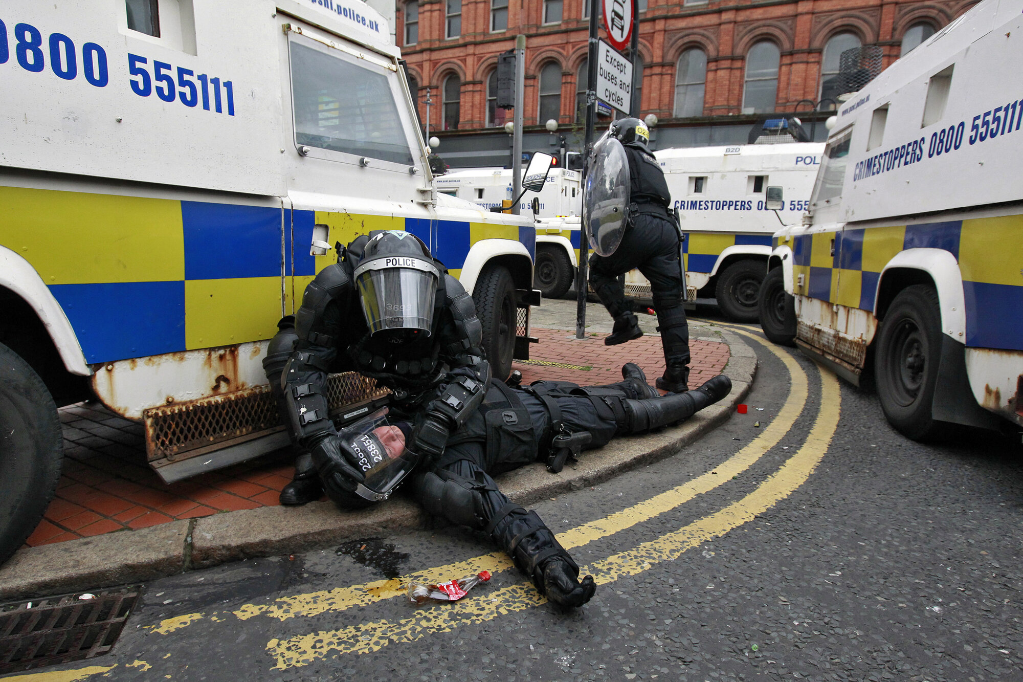 A police officer is tended to by a colleague after Loyalist protesters attacked the police with bricks and bottles as they waited for a Republican parade to make its way through Belfast City Centre, 2013.