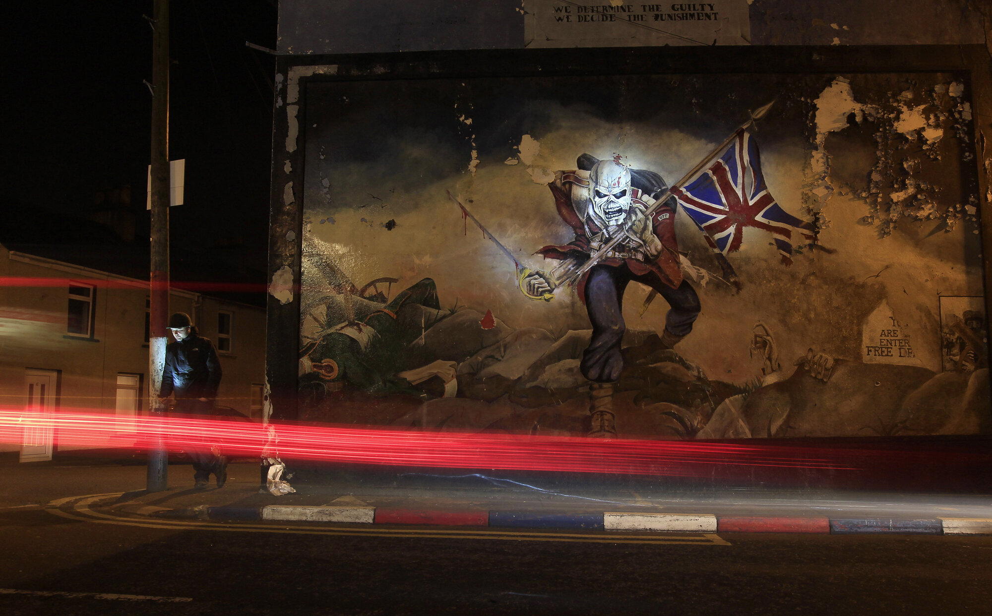 A man checks his mobile phone beside a loyalist paramilitary mural in the Waterside area of Derry, 2013.